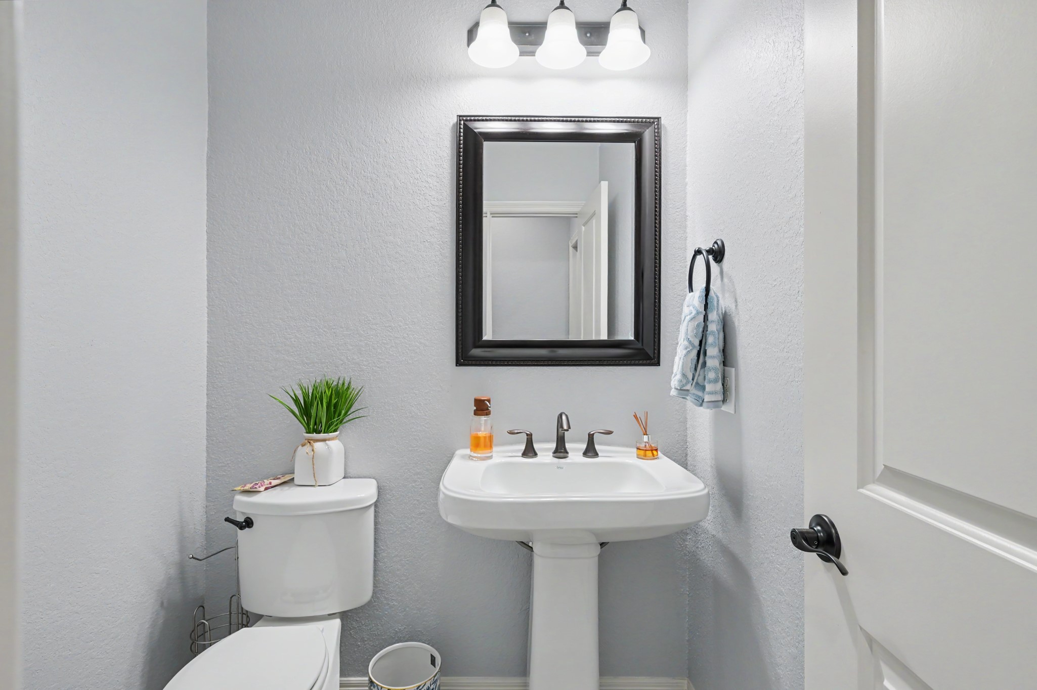 Charming powder room featuring a pedestal sink, sleek fixtures, and a stylish framed mirror, perfectly accented by bright lighting and a neutral color palette.