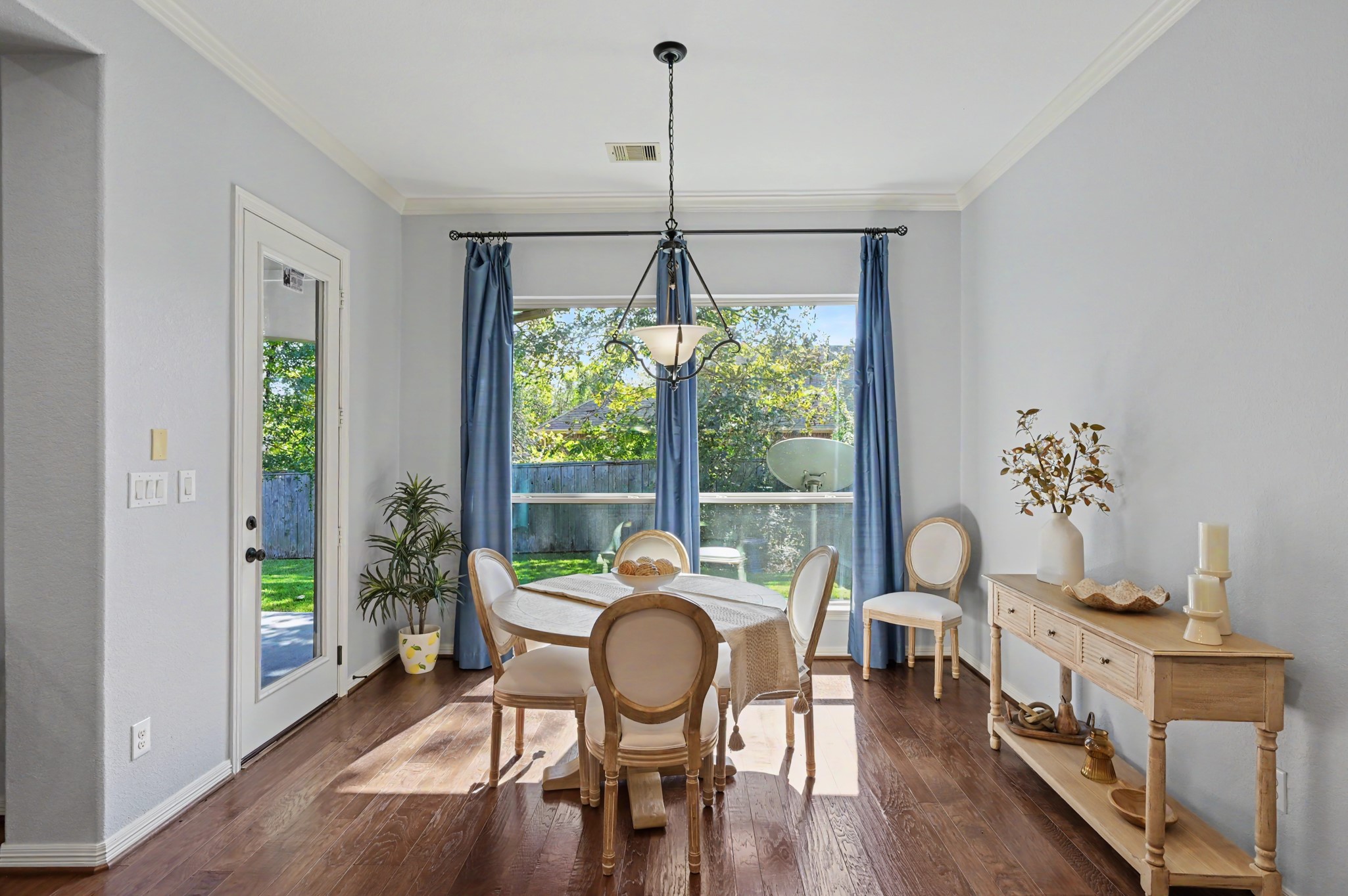 Bright dining area featuring elegant wood flooring and abundant natural light, with a charming view of the backyard through large windows and a glass door.