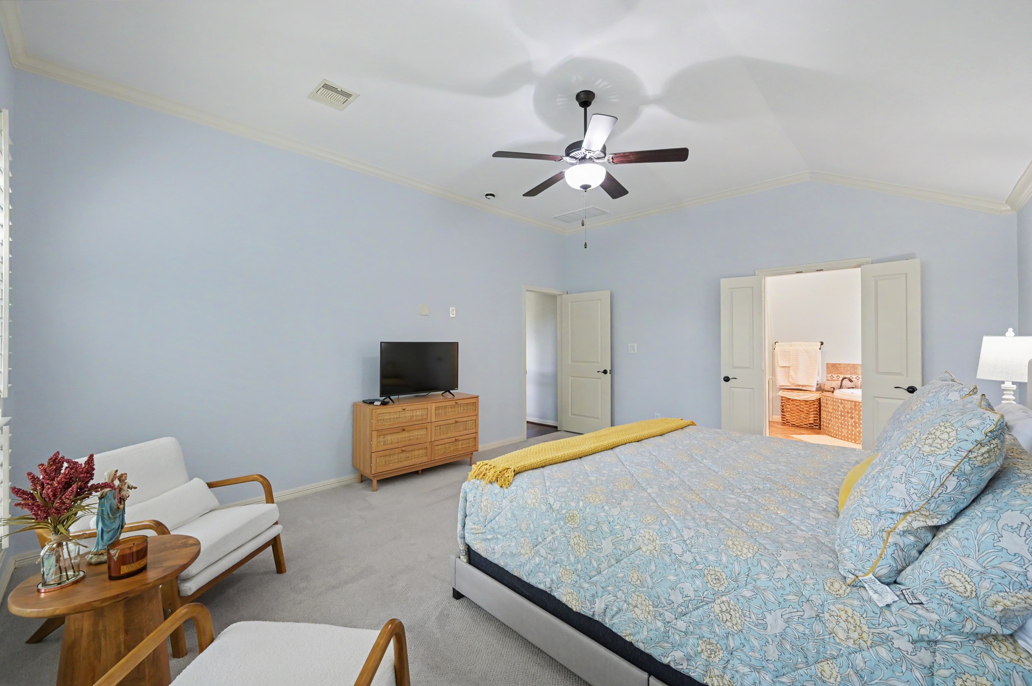 Spacious bedroom with soft blue walls, featuring a cozy sitting area, elegant ceiling fan, and convenient ensuite bathroom access through double doors.