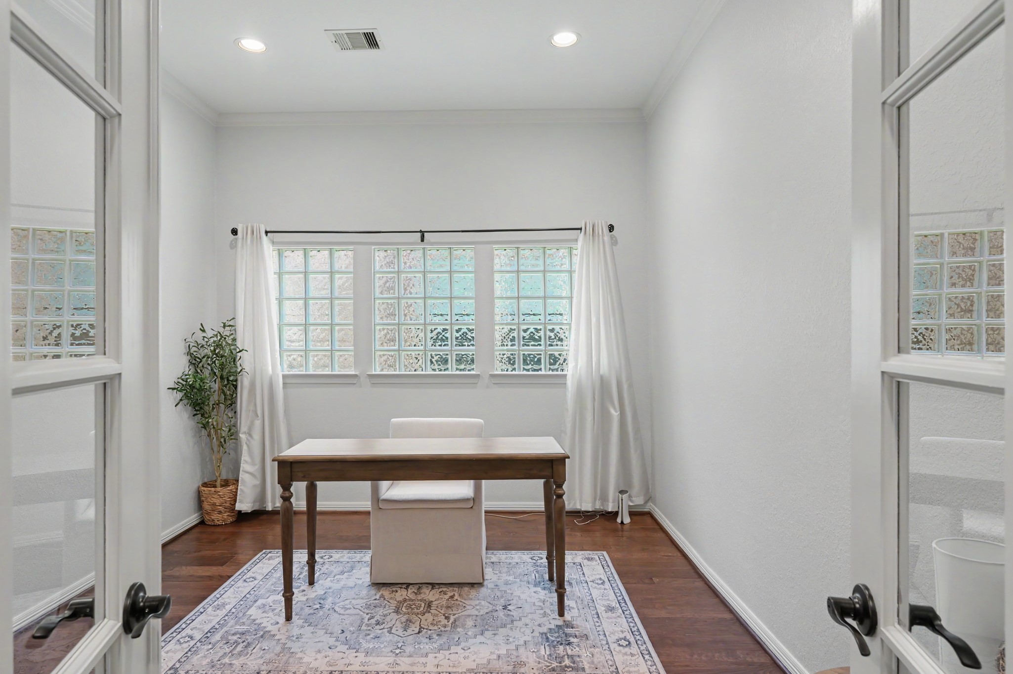Bright and inviting home office with elegant French doors, featuring hardwood floors and a large window offering ample natural light.