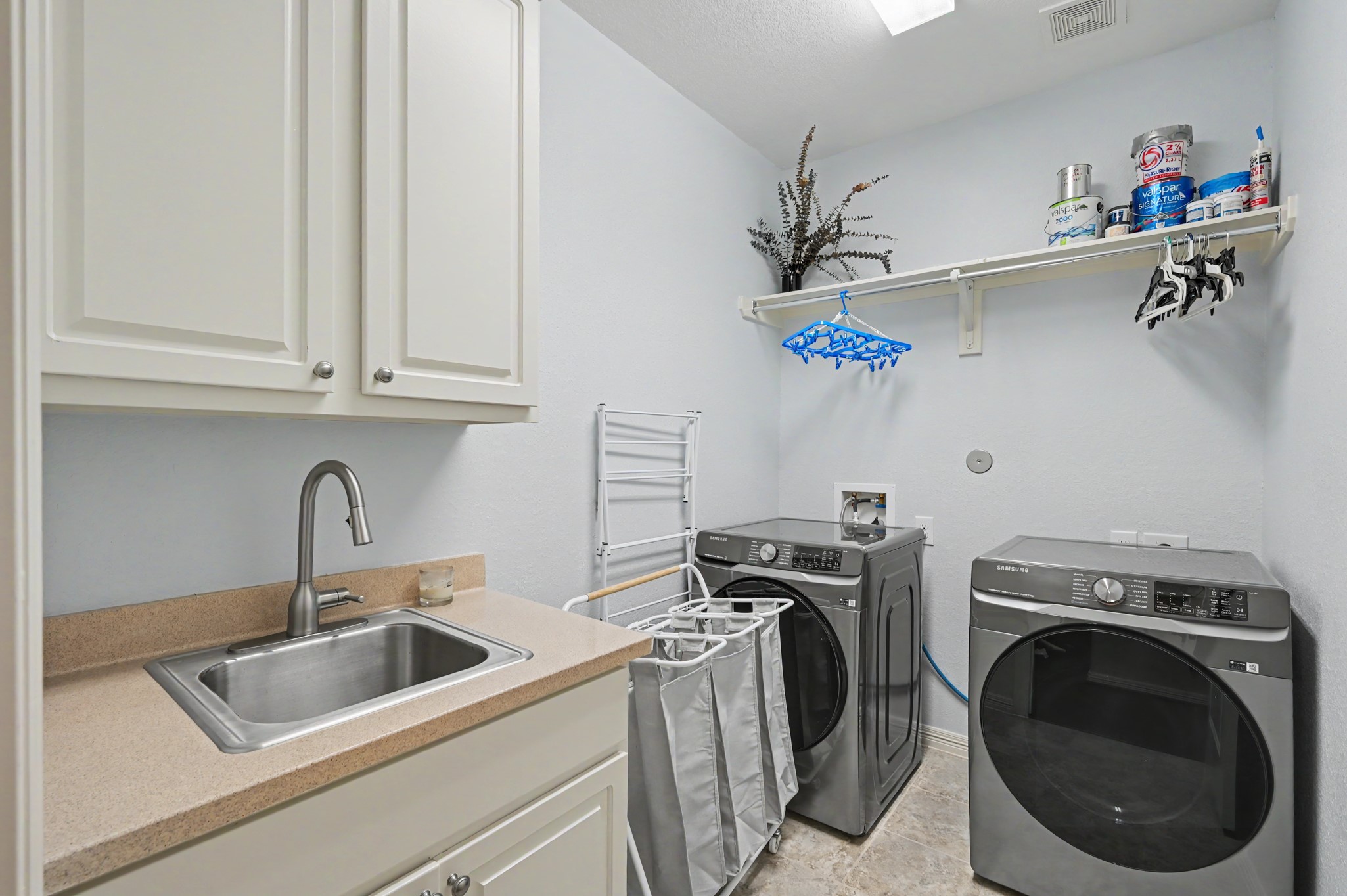 Modern laundry room featuring sleek front-loading washer and dryer, ample cabinetry, and a convenient utility sink for added functionality.