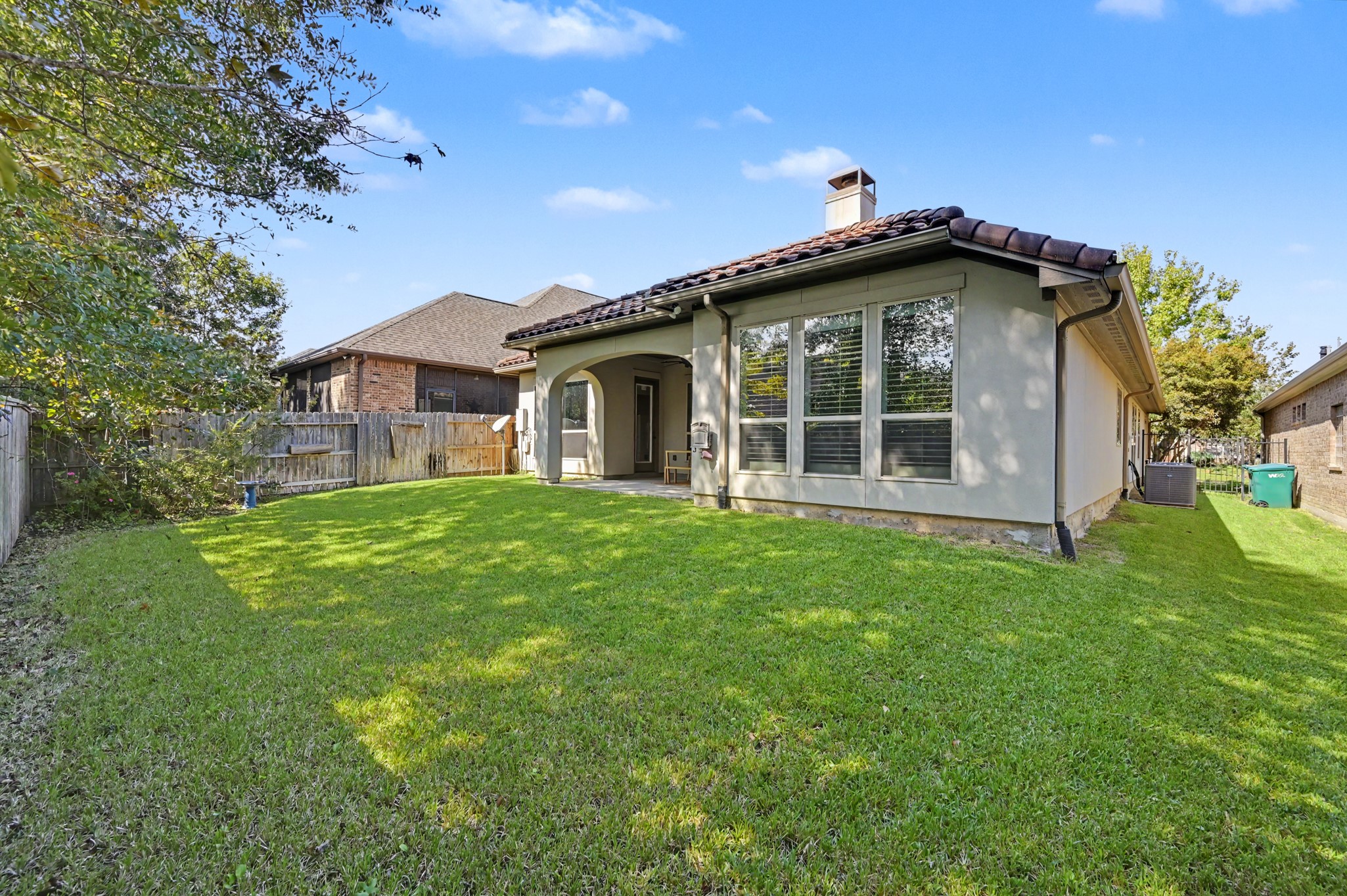 Charming backyard with lush green lawn, perfect for outdoor activities, complemented by a cozy patio with arched openings for relaxation.