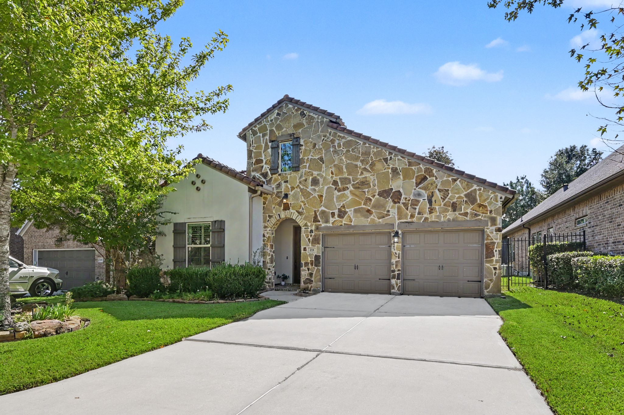 Charming home featuring a beautiful stone facade, a spacious three-car garage, and lush landscaping, set on a serene residential street.