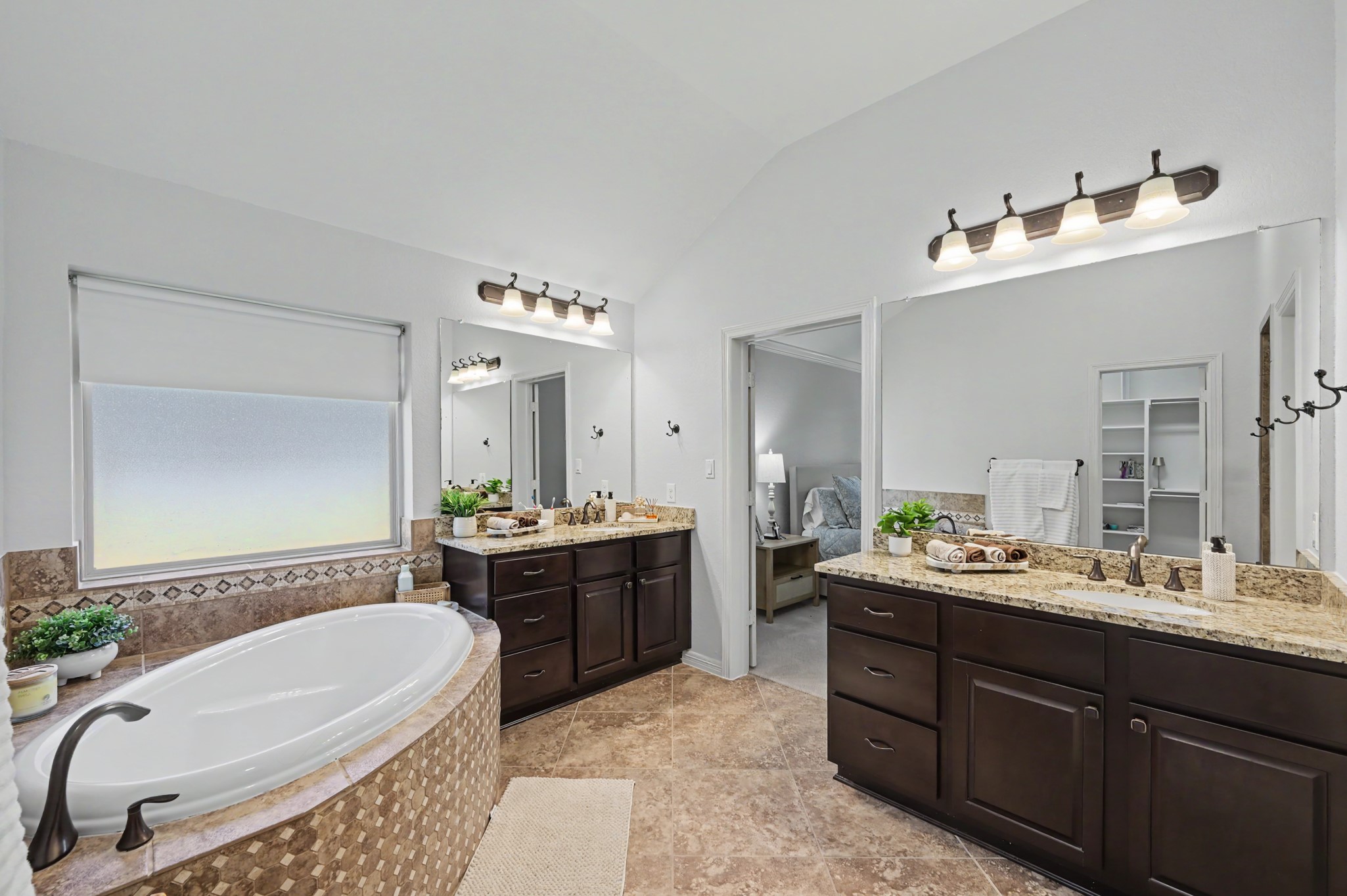 Spacious and elegant bathroom featuring a luxurious soaking tub, dual vanities with granite countertops, and warm wood cabinetry, offering both style and functionality.