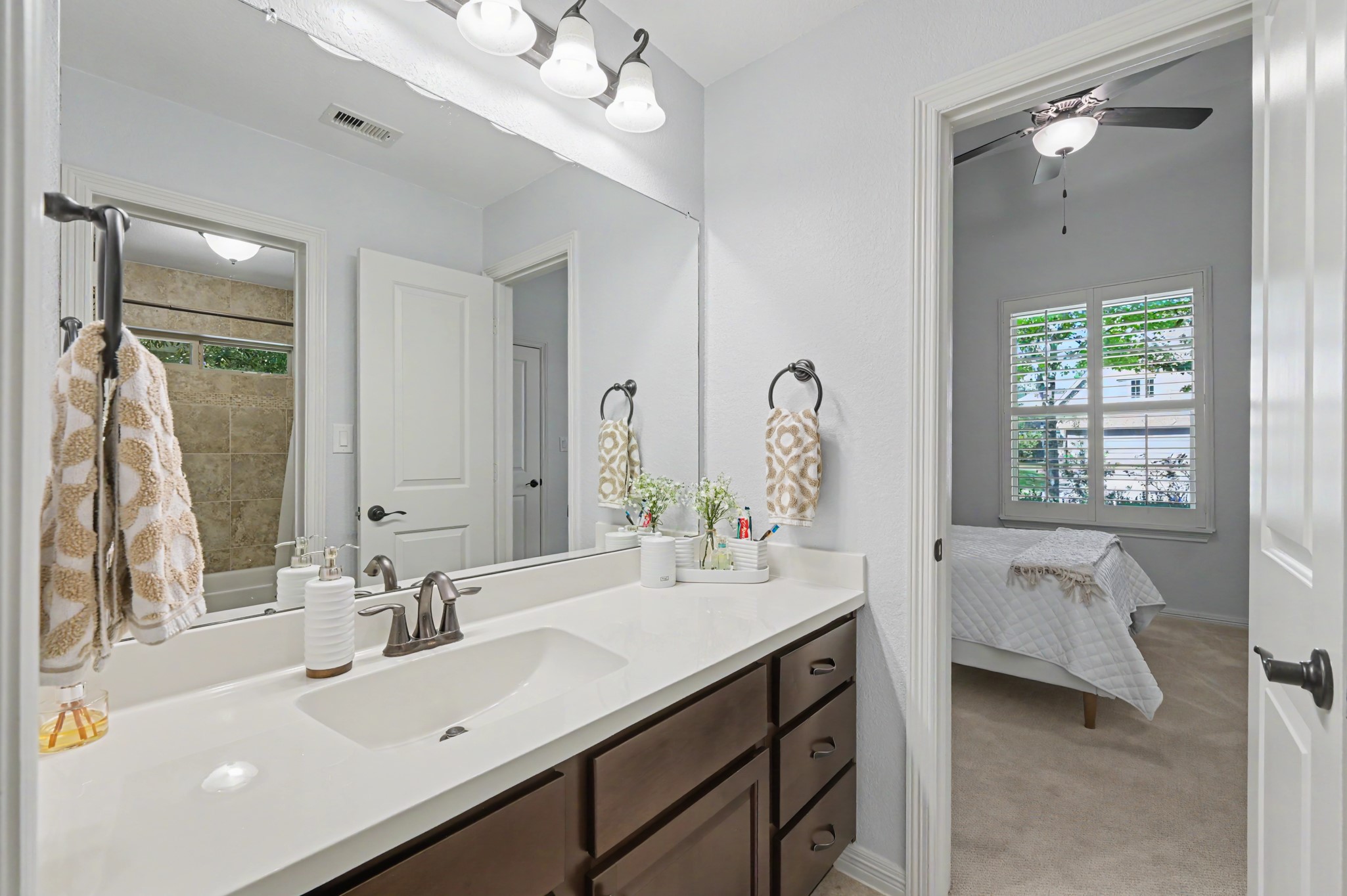 Elegant bathroom featuring a sleek double vanity with dark cabinetry, leading into a cozy bedroom with natural light streaming through plantation shutters.