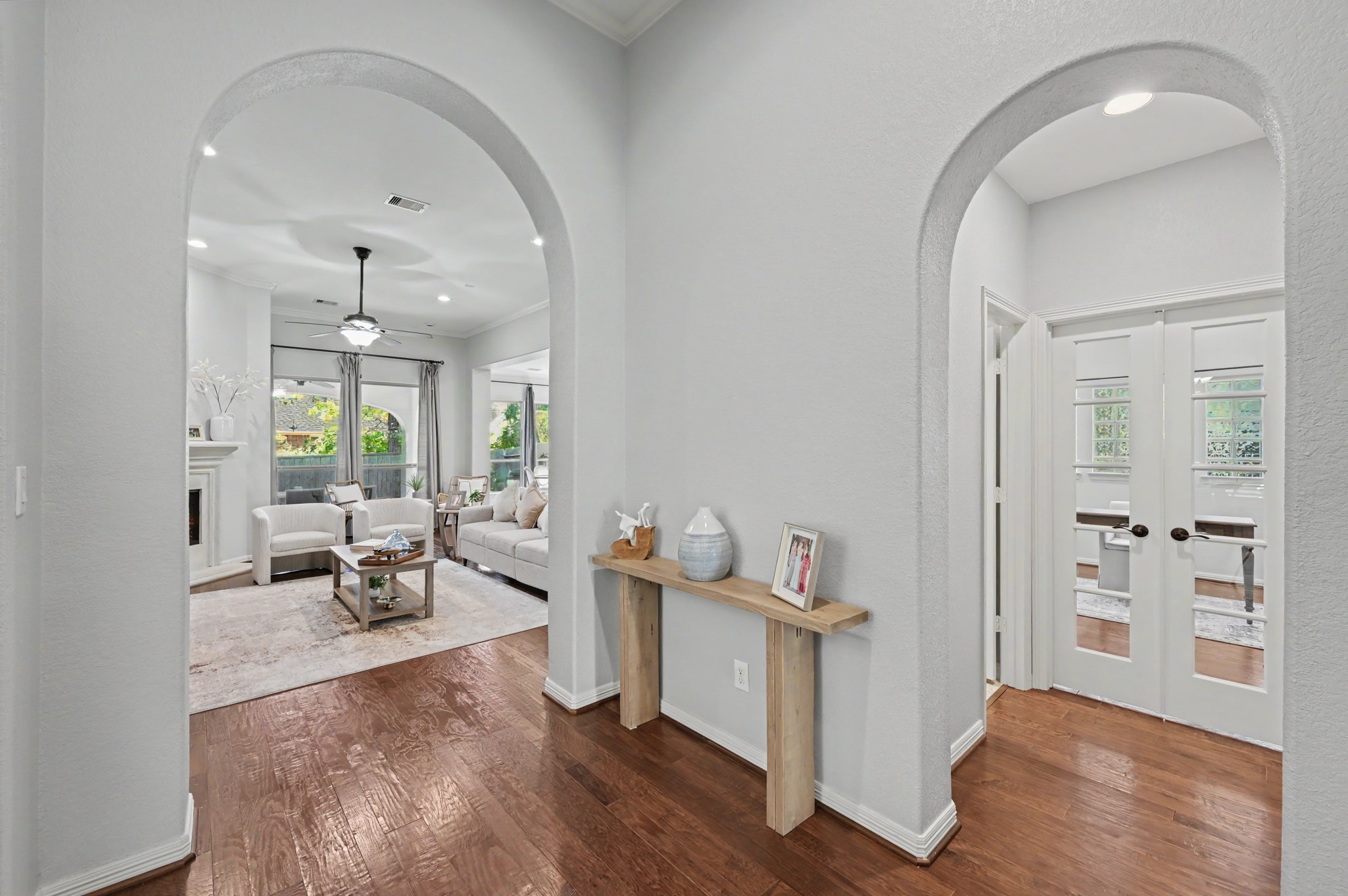 Elegant entryway featuring arched doorways leading to a bright living room with hardwood floors and a cozy fireplace, complemented by French doors opening to a versatile office space.