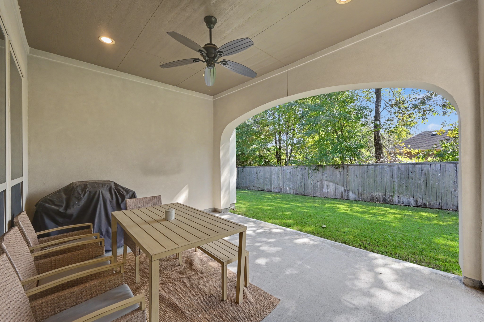 Charming covered patio with ceiling fan, perfect for outdoor dining and relaxation, overlooking a private, fenced backyard with lush greenery.