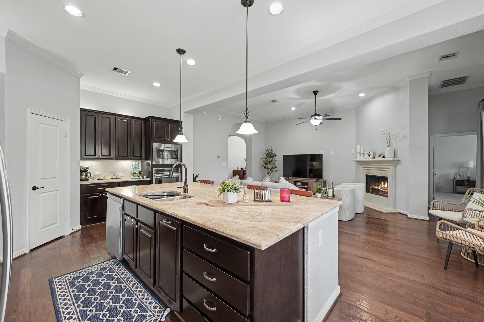 Spacious open-concept living area featuring a modern kitchen with dark cabinetry, a large island, and pendant lighting, seamlessly flowing into a cozy living room with a fireplace and hardwood floors.