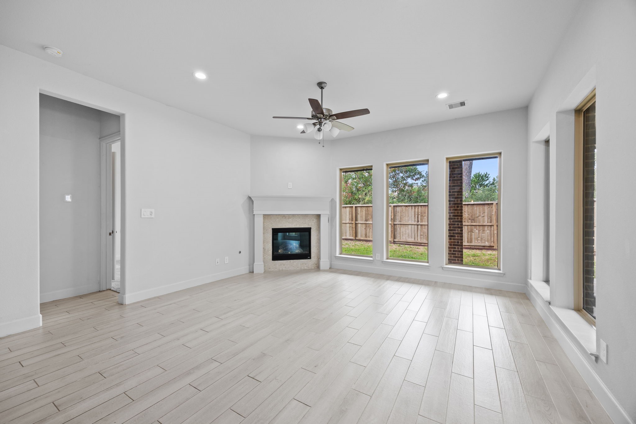 Inviting living space with a fireplace, ceiling fan, and picturesque backyard views.