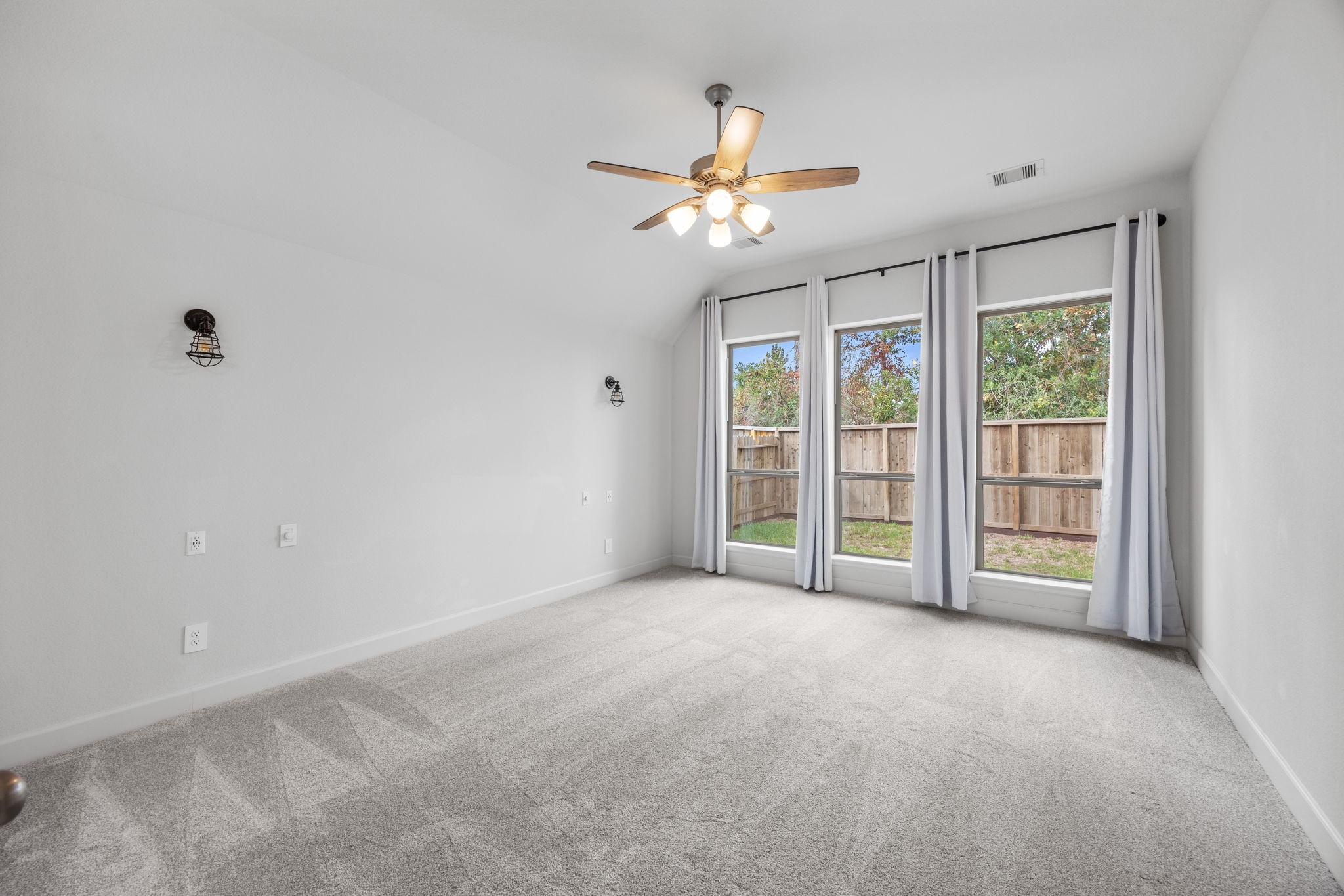 Spacious bedroom featuring a ceiling fan, beautiful flooring, and a wall of windows overlooking the outdoors.