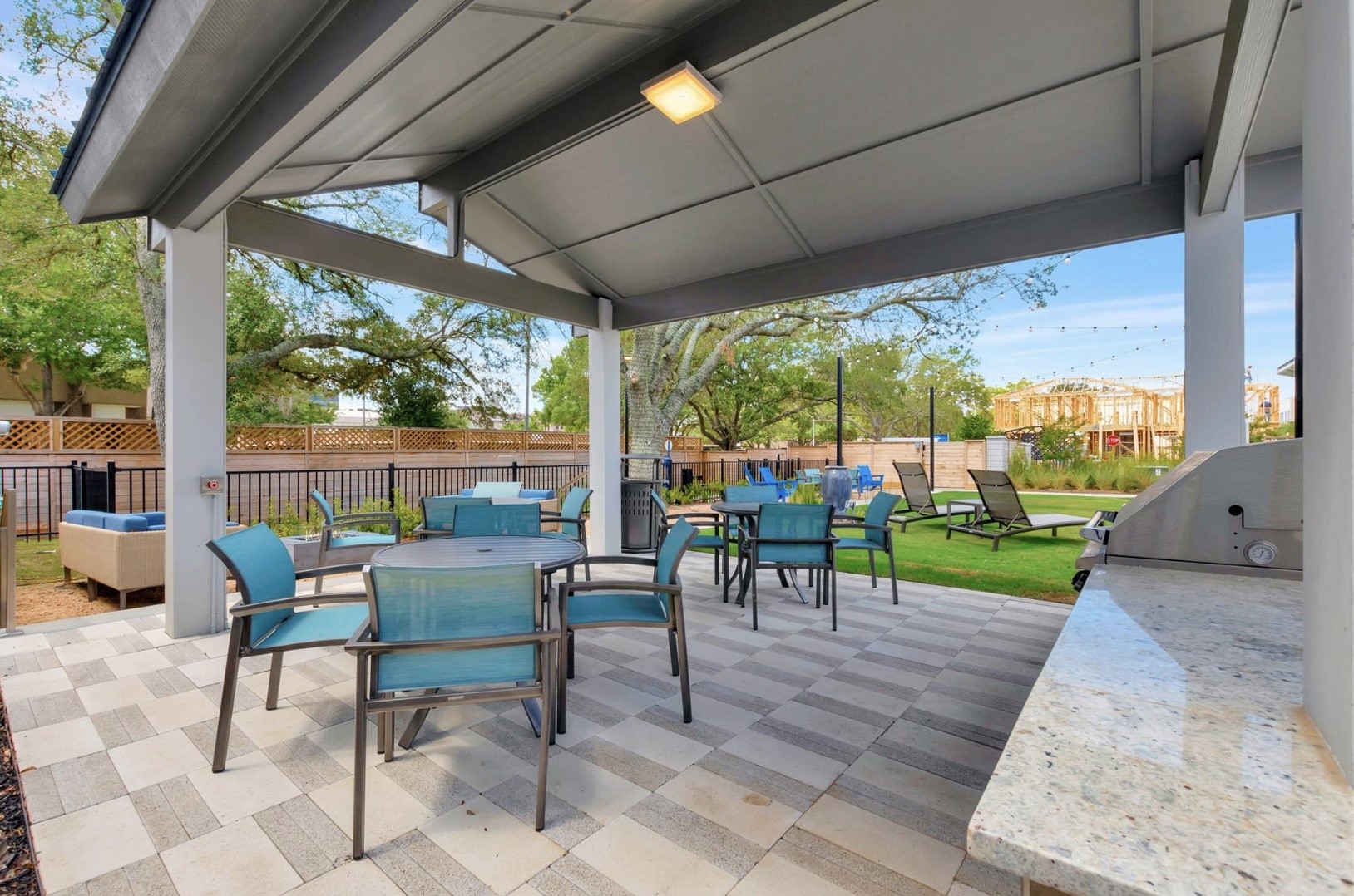 Enjoy an outdoor meal at the community pavilion, featuring covered tables, seating, and a built-in grill with counter space for serving.