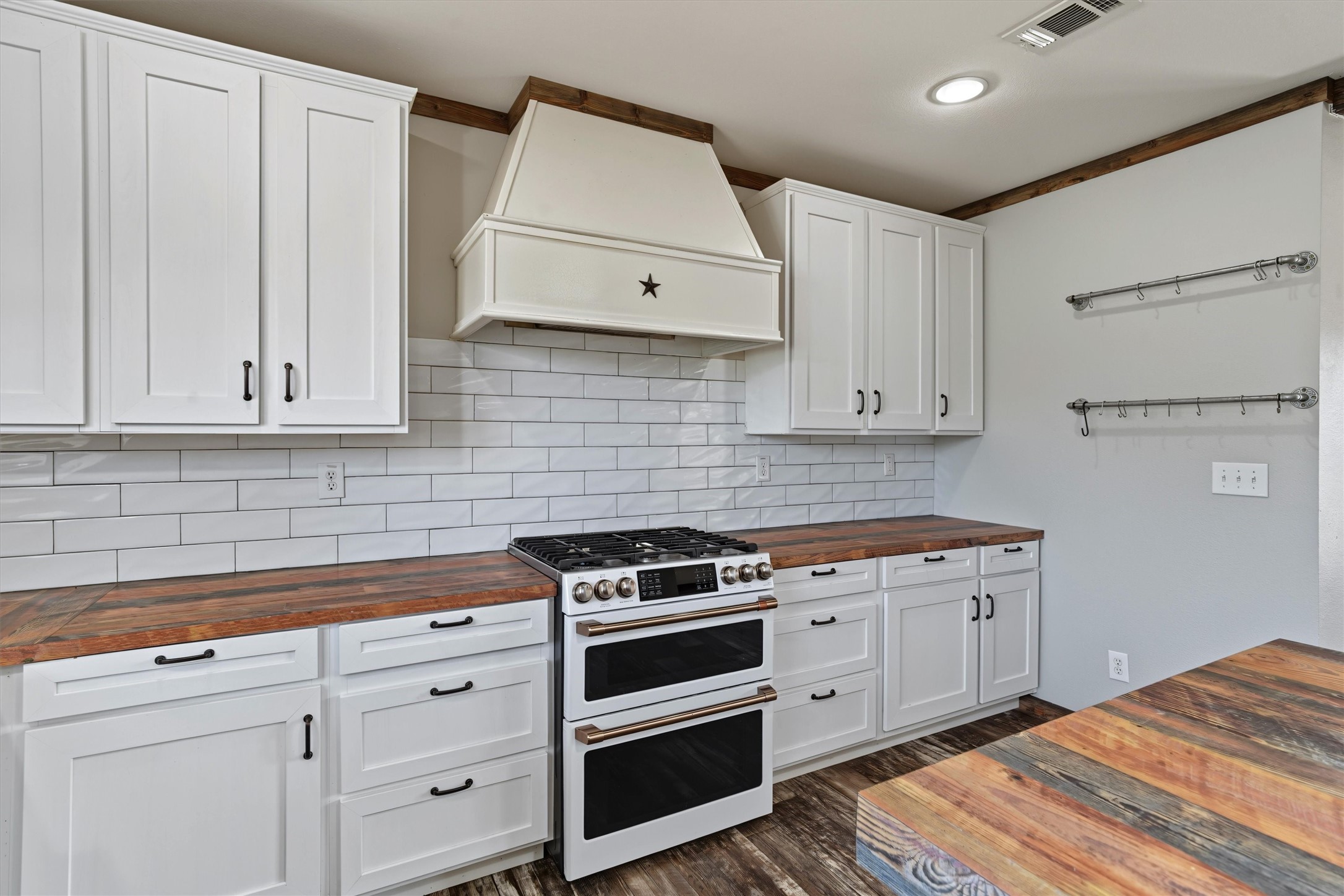 This white kitchen is stunning with its double oven, tile backsplash, and accent range hood. Notice the pots and pan drawers