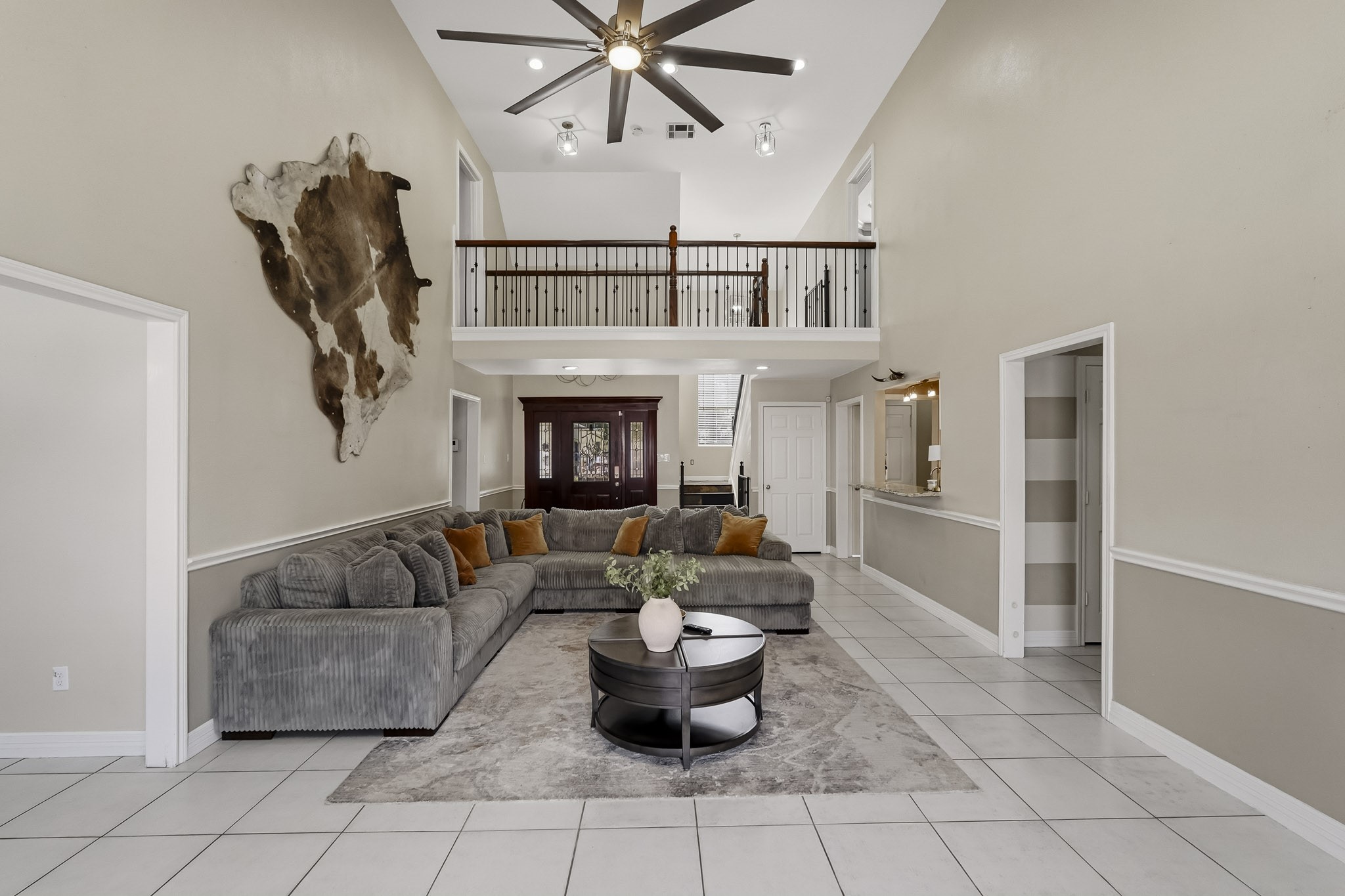 Spacious living area with high ceilings and a modern fan, featuring a cozy sectional sofa and stylish decor. A second-floor balcony overlooks the room, adding to the open, airy feel. Spacious living area with high ceilings and a modern fan, featuring a cozy sectional sofa and stylish decor. A second-floor balcony overlooks the room, adding to the open, airy feel.