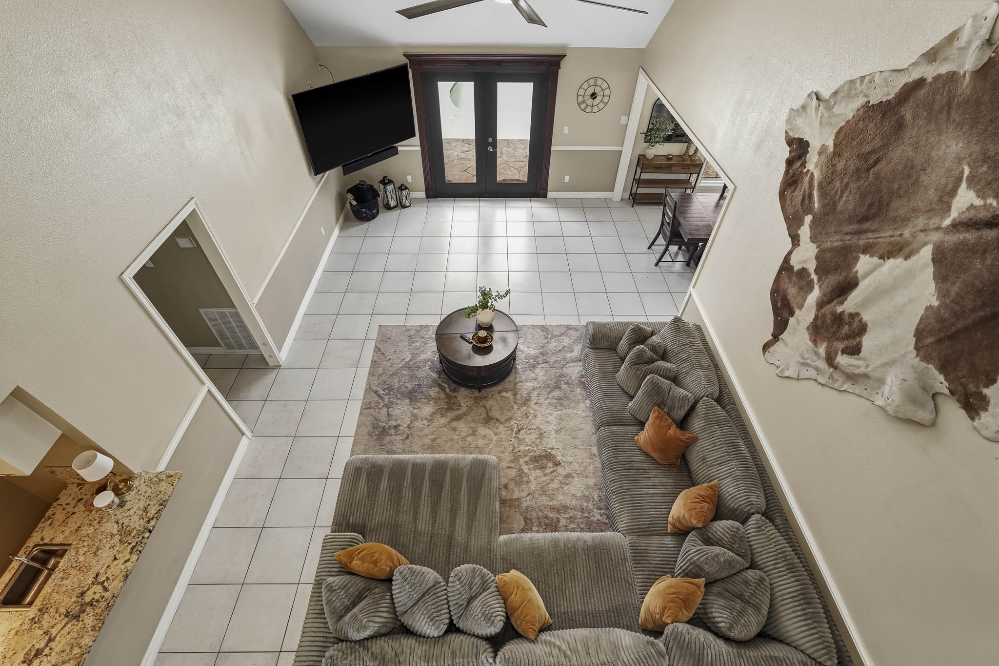 Spacious living area with high ceilings, featuring a cozy sectional sofa and modern decor. Large double doors lead to a bright and inviting outdoor space.