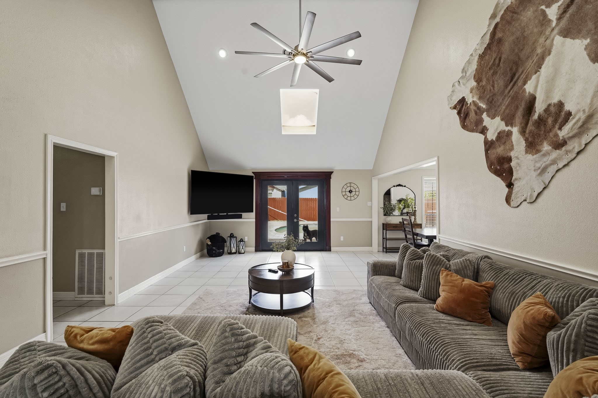 Spacious living room with vaulted ceilings, a modern ceiling fan, and natural light from a skylight. Sliding glass doors lead to an outdoor space that features a beautiful pool, enhancing indoor-outdoor living. Spacious living room with vaulted ceilings, a modern ceiling fan, and natural light from a skylight. Sliding glass doors lead to an outdoor space that features a beautiful pool, enhancing indoor-outdoor living.