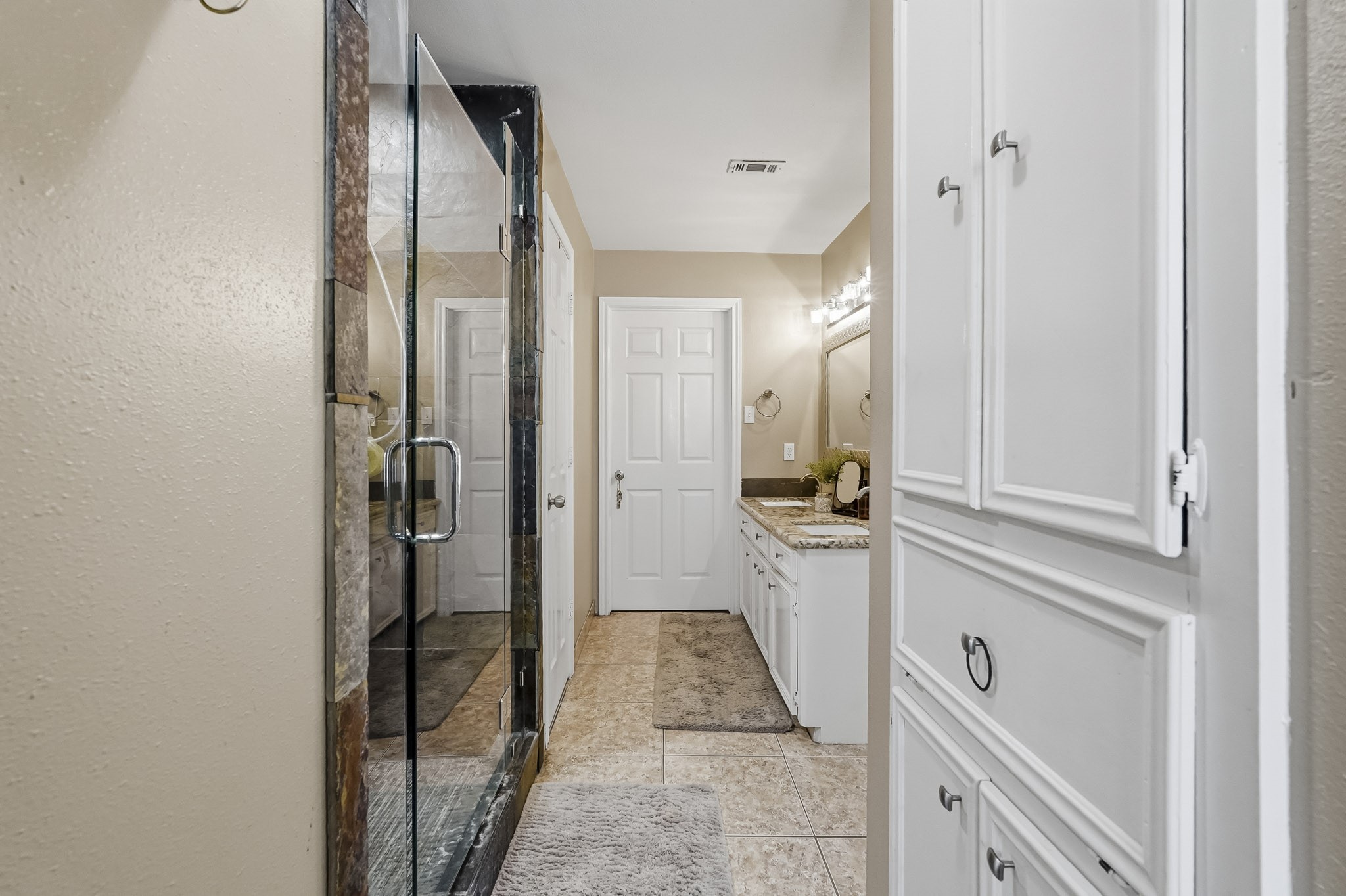 Primary bathroom featuring a spacious glass-enclosed shower, stylish countertop, and ample cabinet storage for a refined touch.