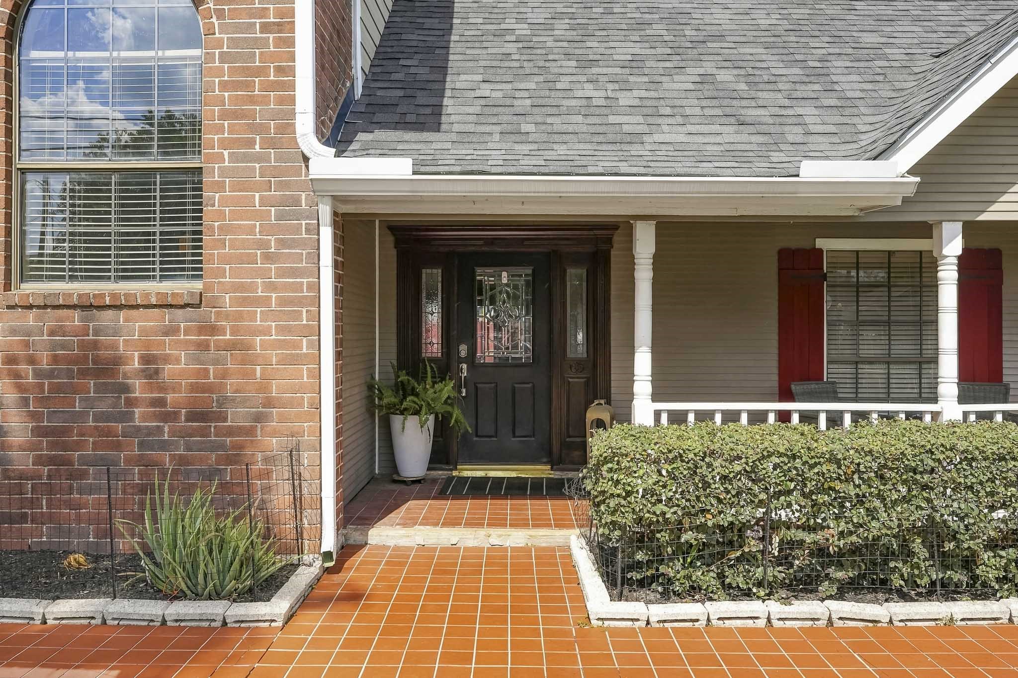 Charming entryway with a welcoming front porch, elegant black door, and vibrant red shutters, complemented by a lush hedge and tasteful brickwork. Charming entryway with a welcoming front porch, elegant black door, and vibrant red shutters, complemented by a lush hedge and tasteful brickwork.