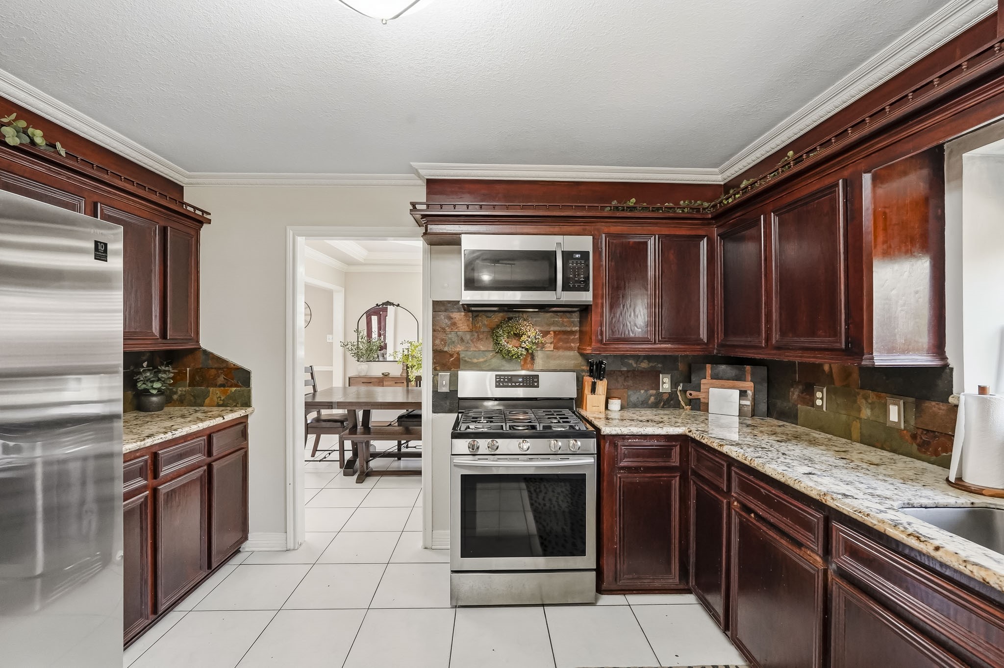 Elegant kitchen featuring rich wood cabinetry, sleek stainless steel appliances, and granite countertops, with a view into the inviting dining area.