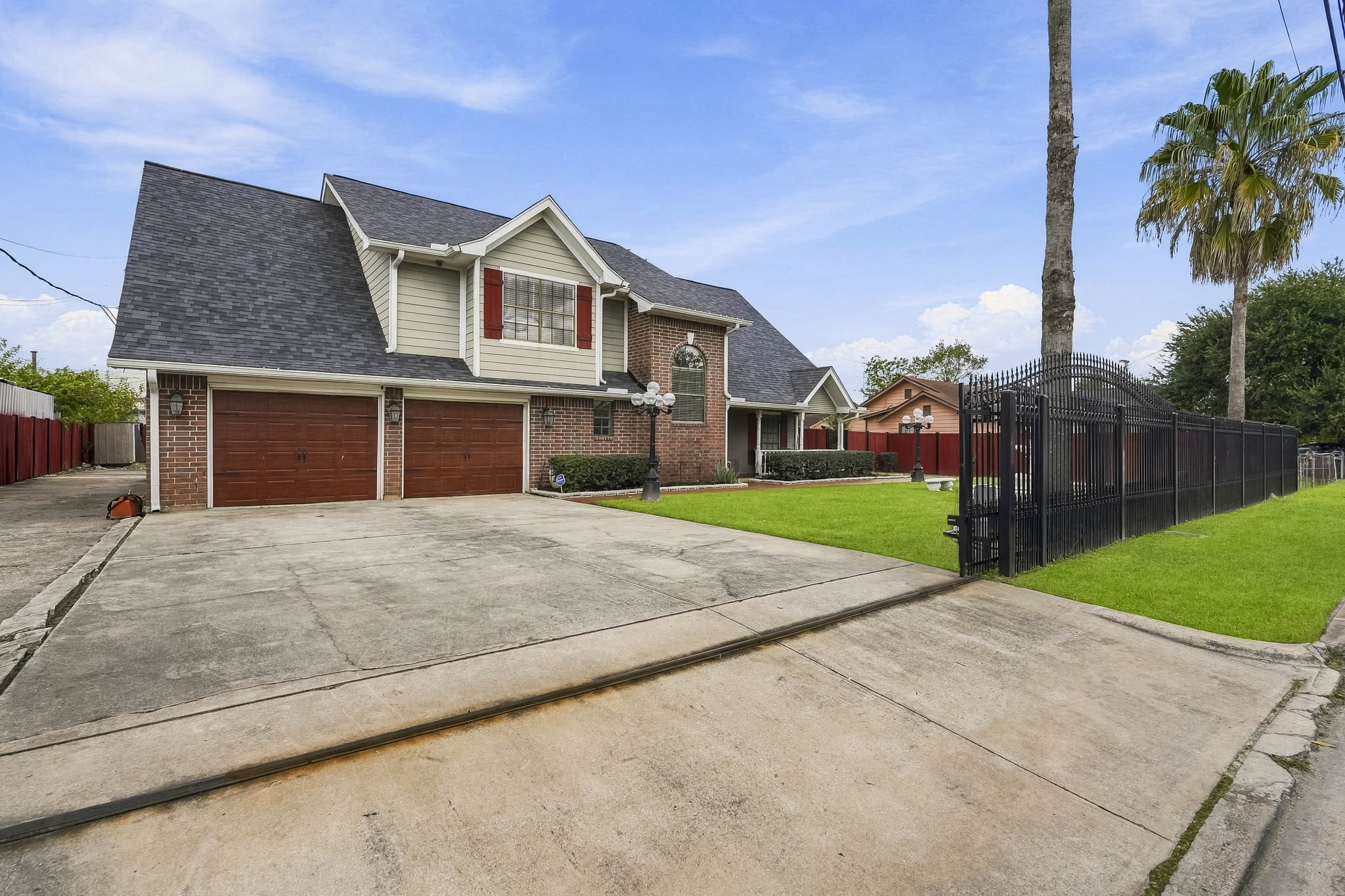 Stunning brick home featuring a spacious driveway leading to a two-car garage, complemented by a well-manicured lawn and secure gated entry.