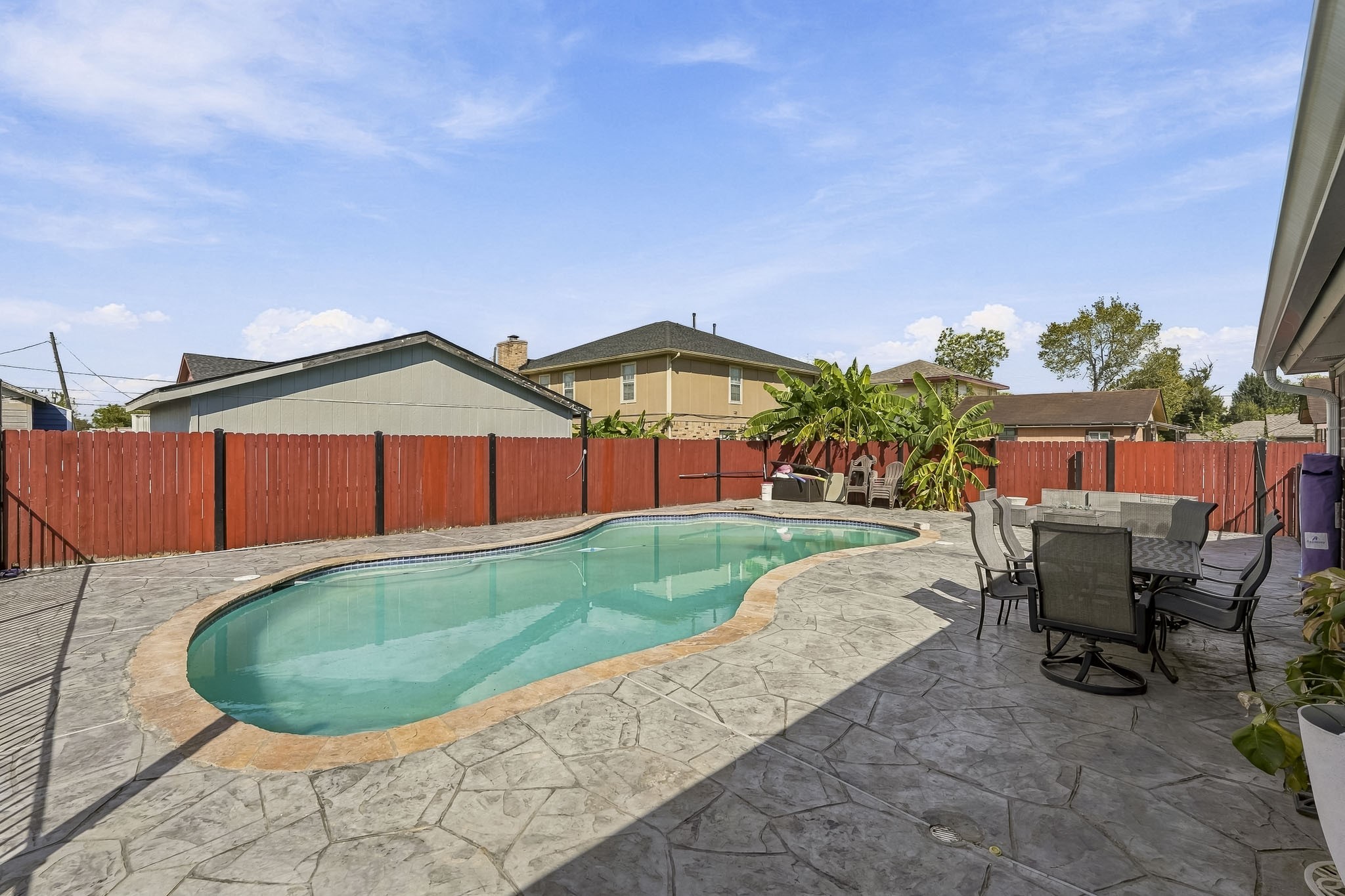 Enjoy sunny days in this spacious backyard featuring a sparkling pool, surrounded by a stylish stamped concrete patio and a vibrant red fence for privacy. Perfect for outdoor dining and relaxation.