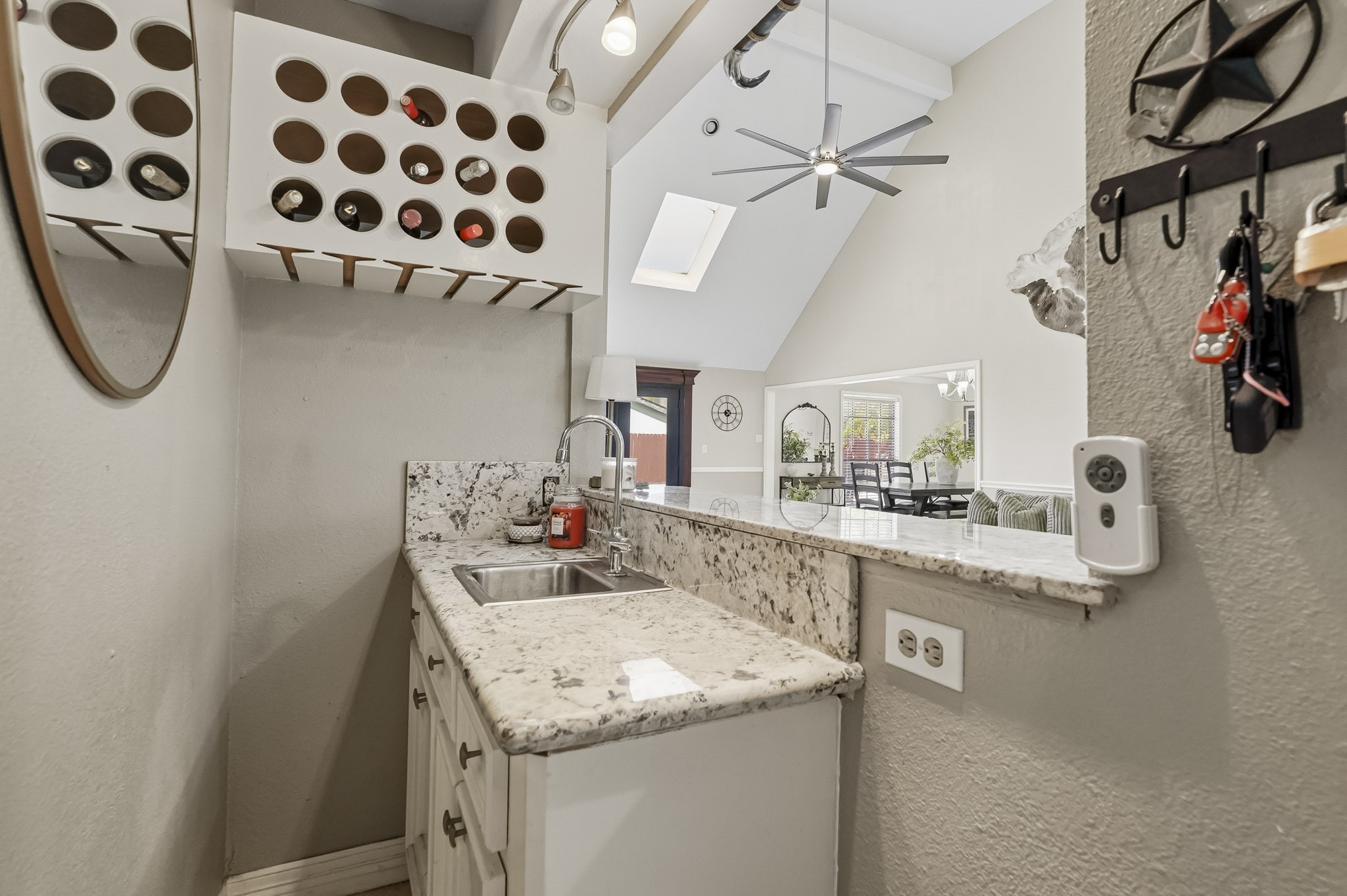 Charming wet bar area with granite countertops, wine storage, and a modern sink, seamlessly opens to a bright living space with vaulted ceilings and skylights.