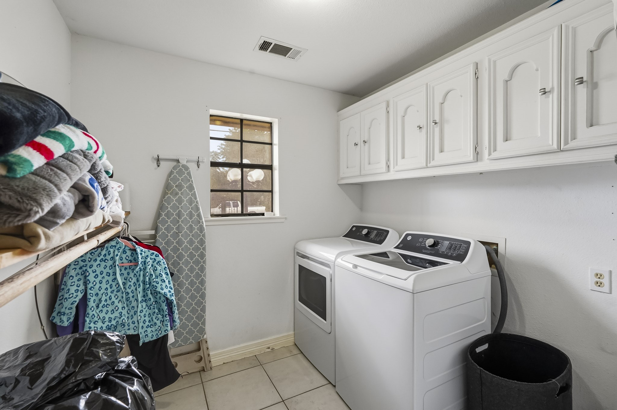 Spacious laundry room with modern washer and dryer, ample storage in overhead cabinets, and convenient hanging space.