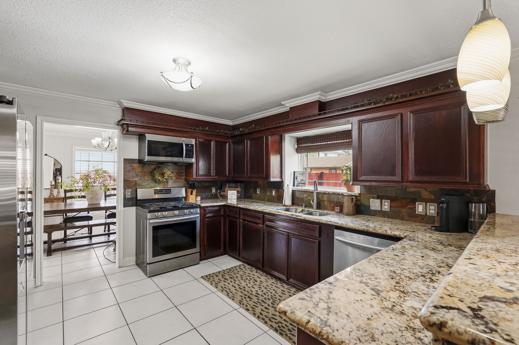 Elegant kitchen with rich dark wood cabinetry, granite countertops, and modern stainless steel appliances, seamlessly flowing into a bright dining area.