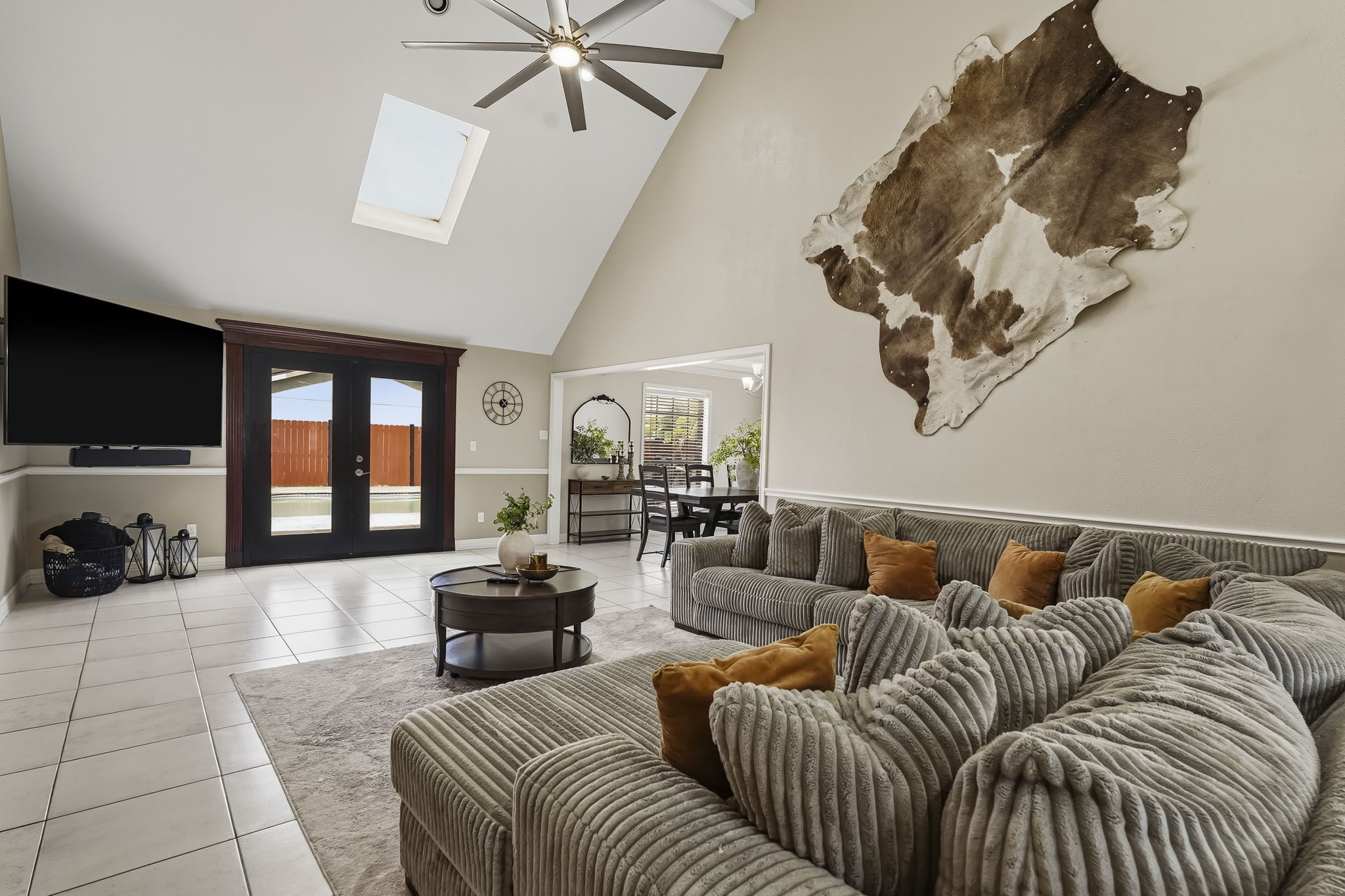 Spacious living room with high ceilings and a skylight. French doors open to the backyard, offering ample natural light and seamless indoor-outdoor living.