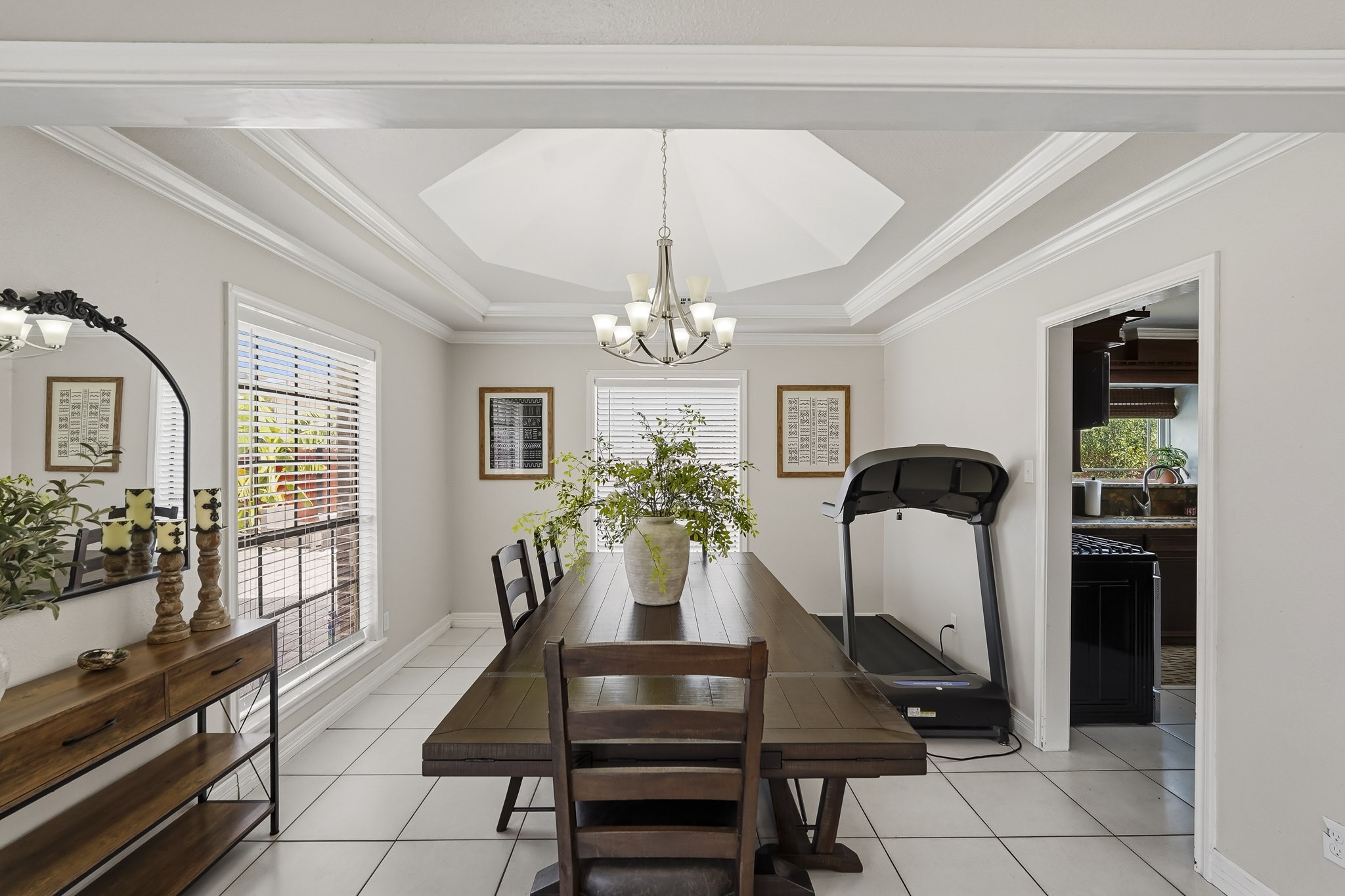 Elegant dining area with a coffered ceiling, stylish chandelier, and abundant natural light from large windows.