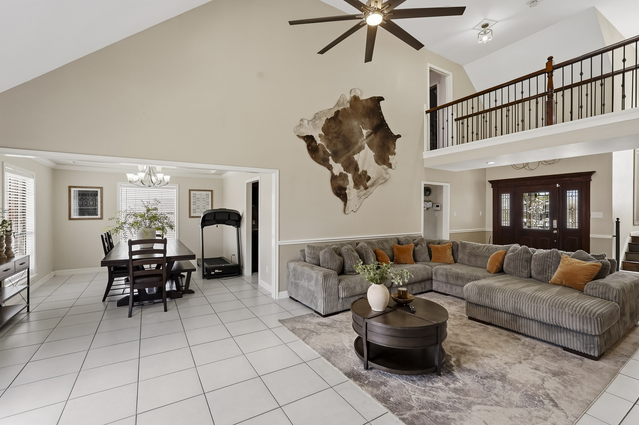 Spacious open-concept living area with high ceilings, featuring a cozy sectional sofa, elegant dining space, and a stylish balcony overlooking the room.