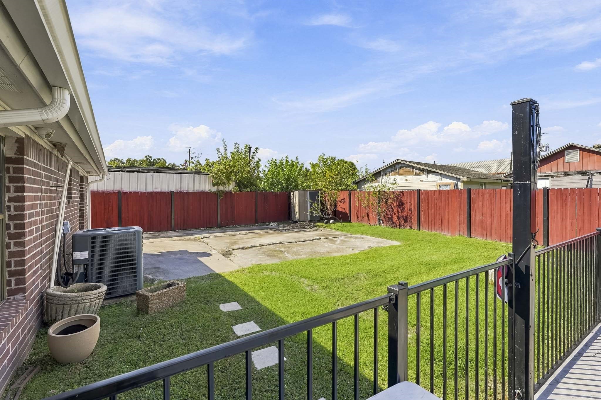 Charming backyard with a spacious lawn, red wooden fence, and patio area, perfect for outdoor entertaining and relaxation.