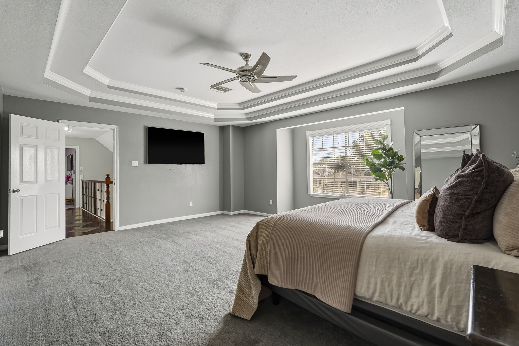 Spacious primary bedroom featuring a stylish tray ceiling, plush carpeting, and abundant natural light from a large window.
