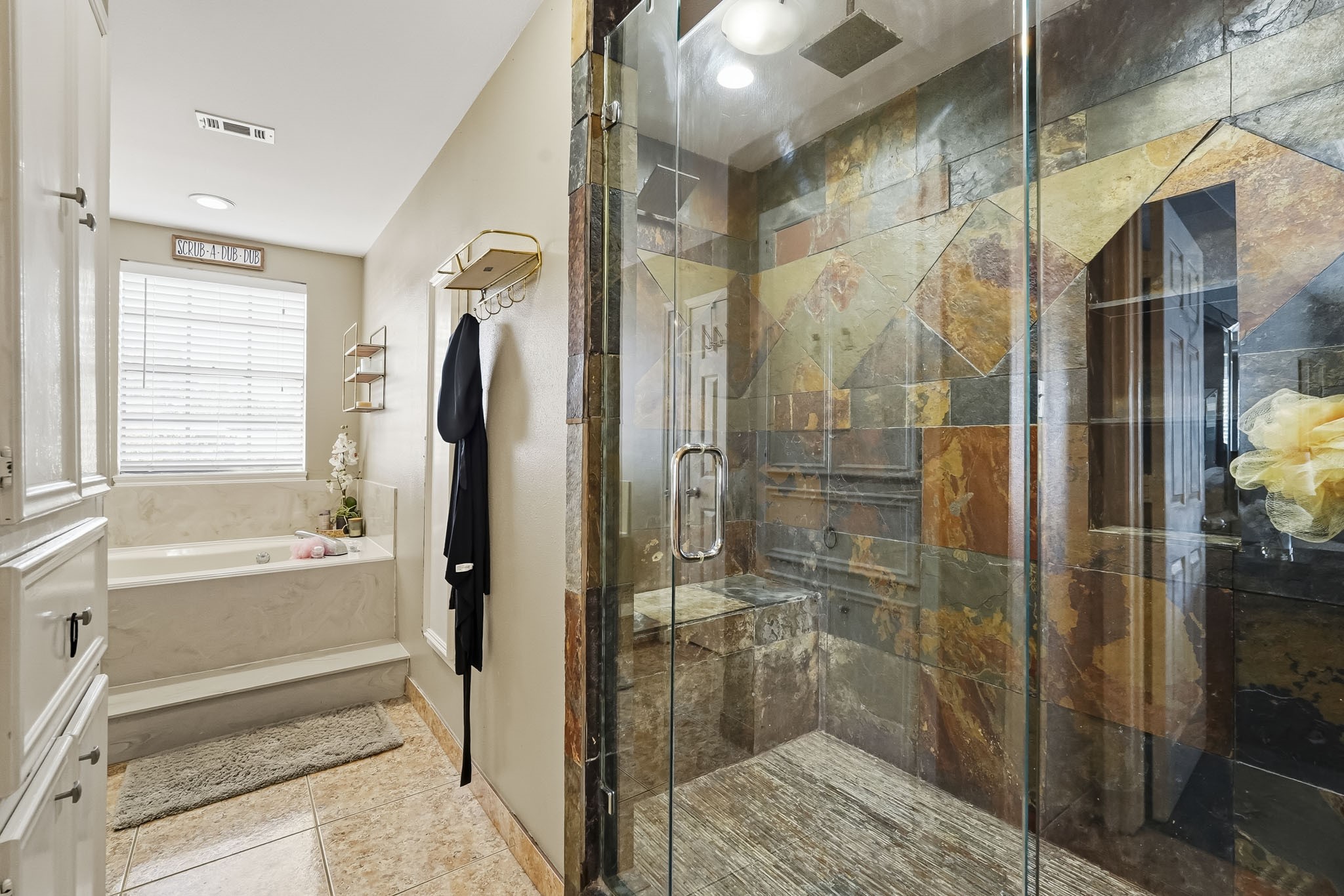 Luxurious bathroom featuring a spacious walk-in shower with unique slate tile design and a serene soaking tub bathed in natural light.