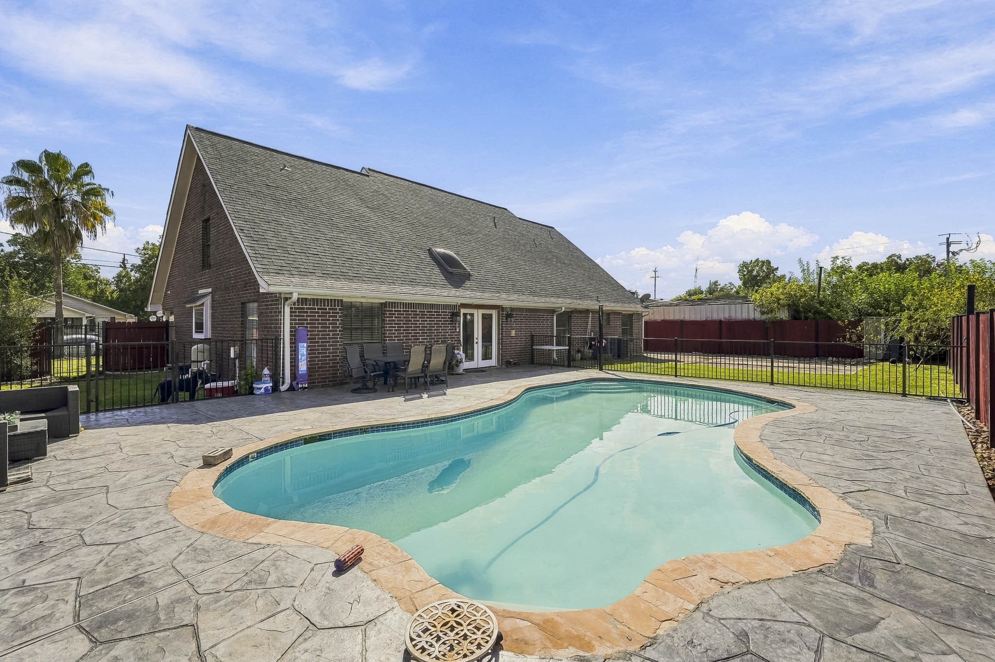 Spacious backyard oasis featuring a sparkling pool, expansive patio, and a charming brick home, perfect for entertaining and relaxation.
