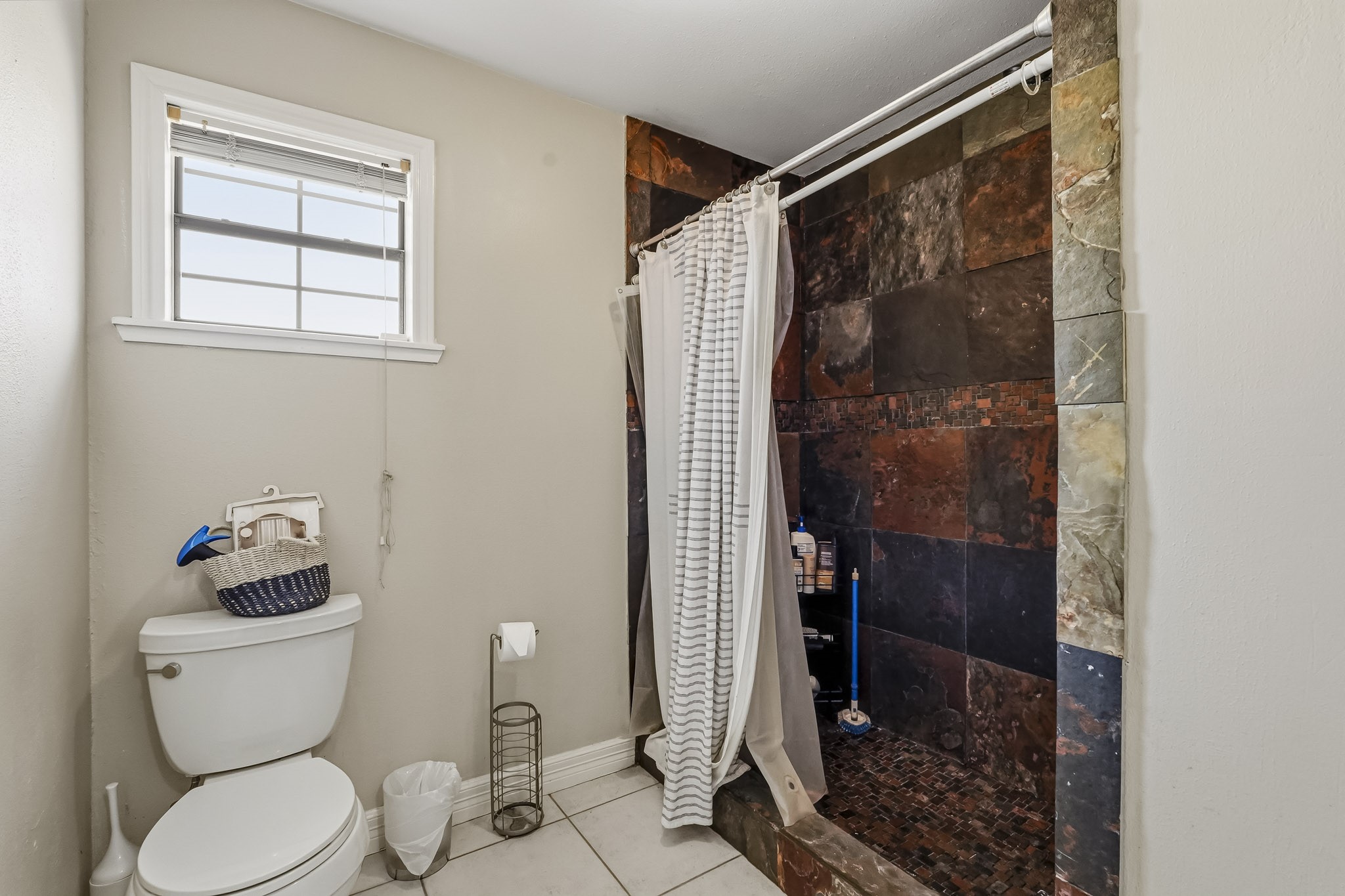 Modern secondary bathroom featuring a spacious walk-in shower with striking dark tile accents, complemented by a convenient toilet and a window for natural light.