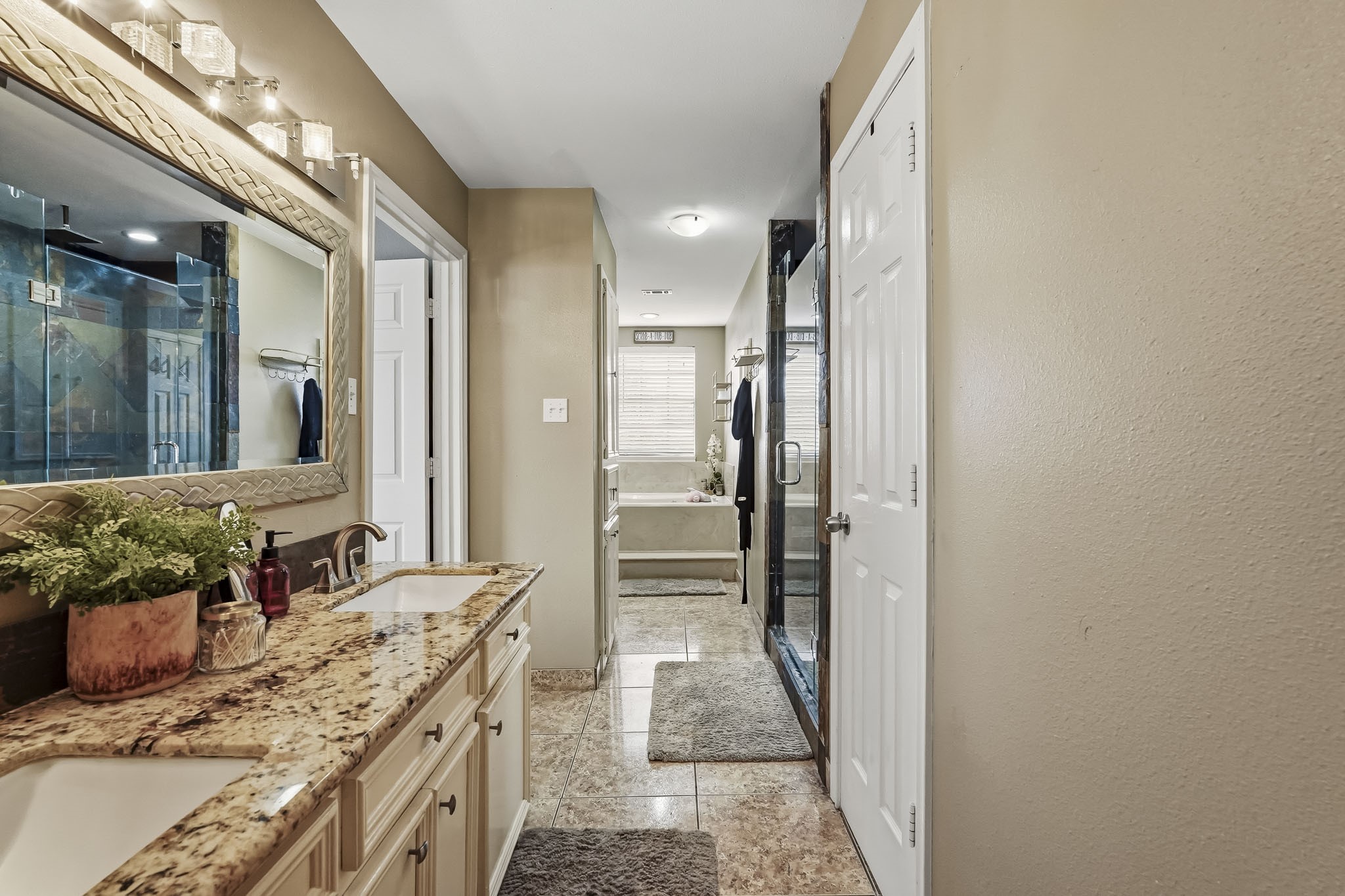 Primary bathroom features spacious double vanity with granite countertops, a large framed mirror, and a luxurious glass-enclosed shower.