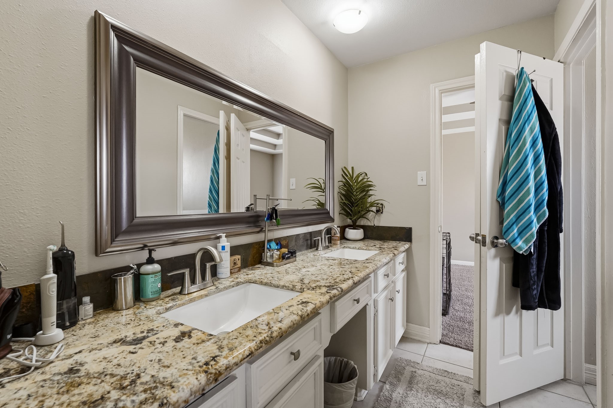 Elegant secondary bathroom featuring a granite countertop with dual sinks, modern fixtures, and ample storage, complemented by a large framed mirror.