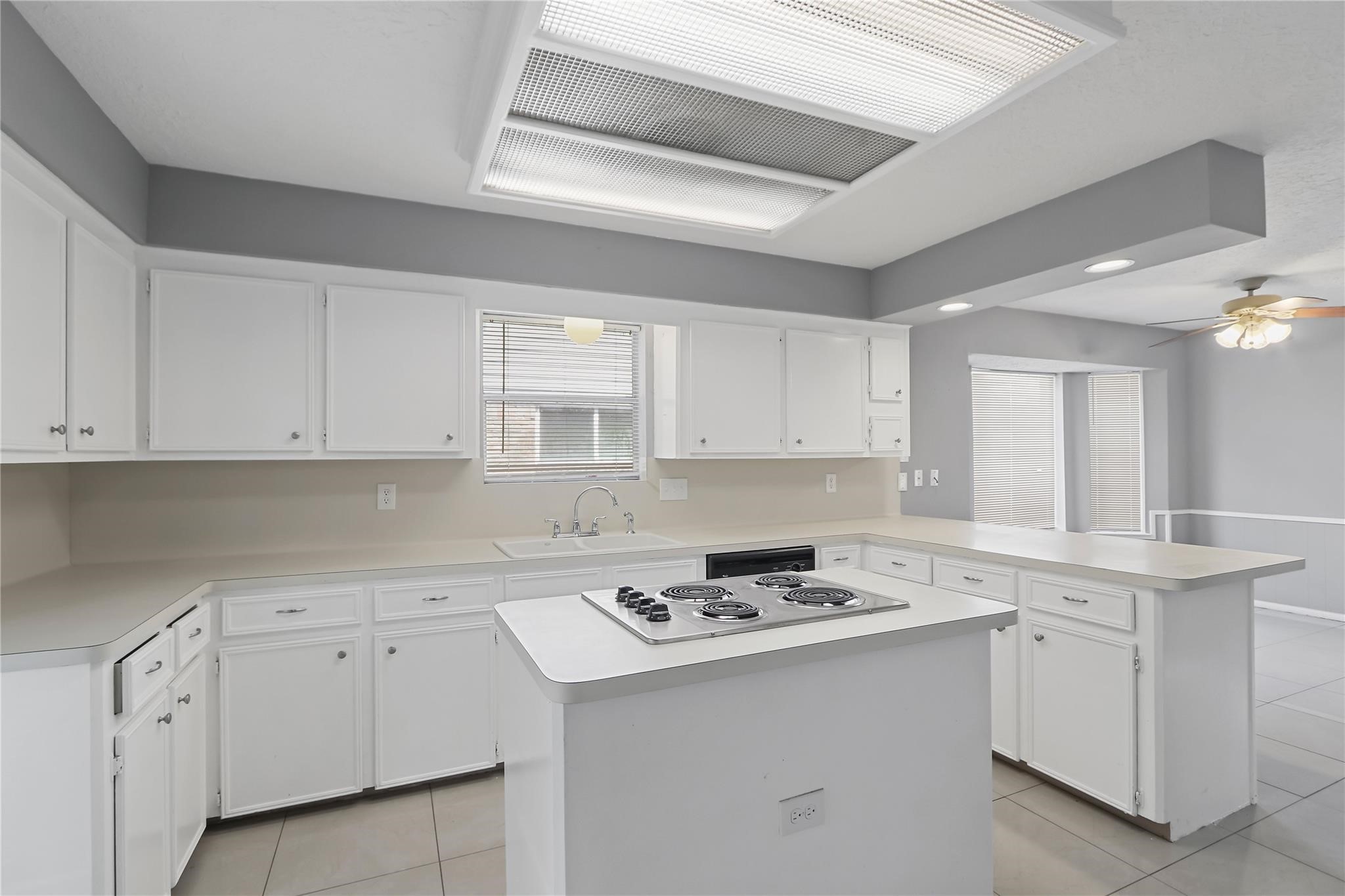 Another view of the kitchen, featuring generous cabinet and counter space, a center island with cooktop, and an open view into the breakfast area.