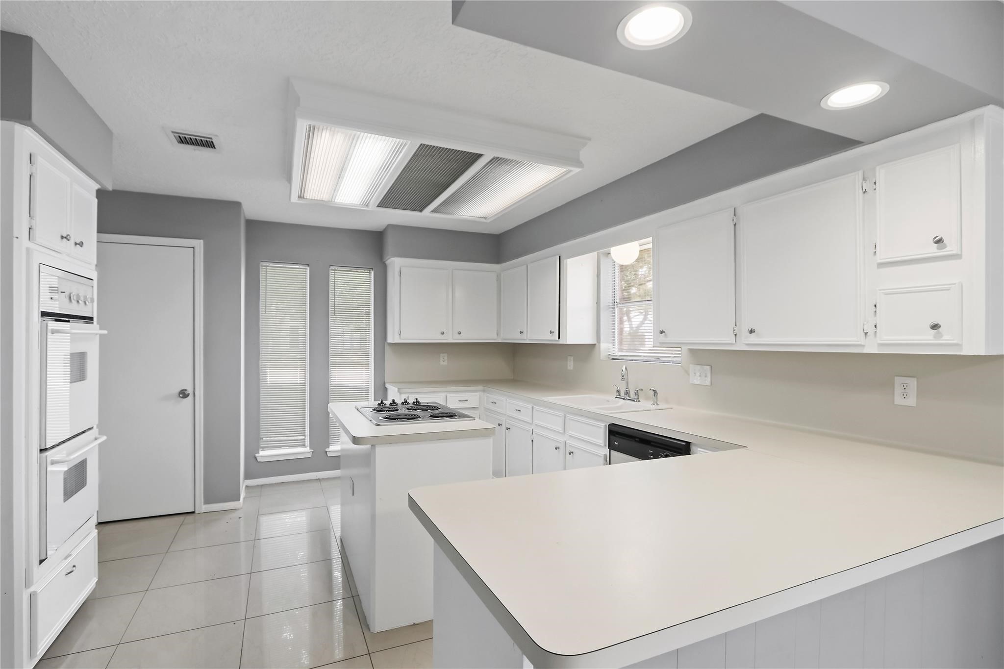 Spacious kitchen featuring white cabinetry, ample counter space, a center island with cooktop, and a breakfast bar overlooking the breakfast area.