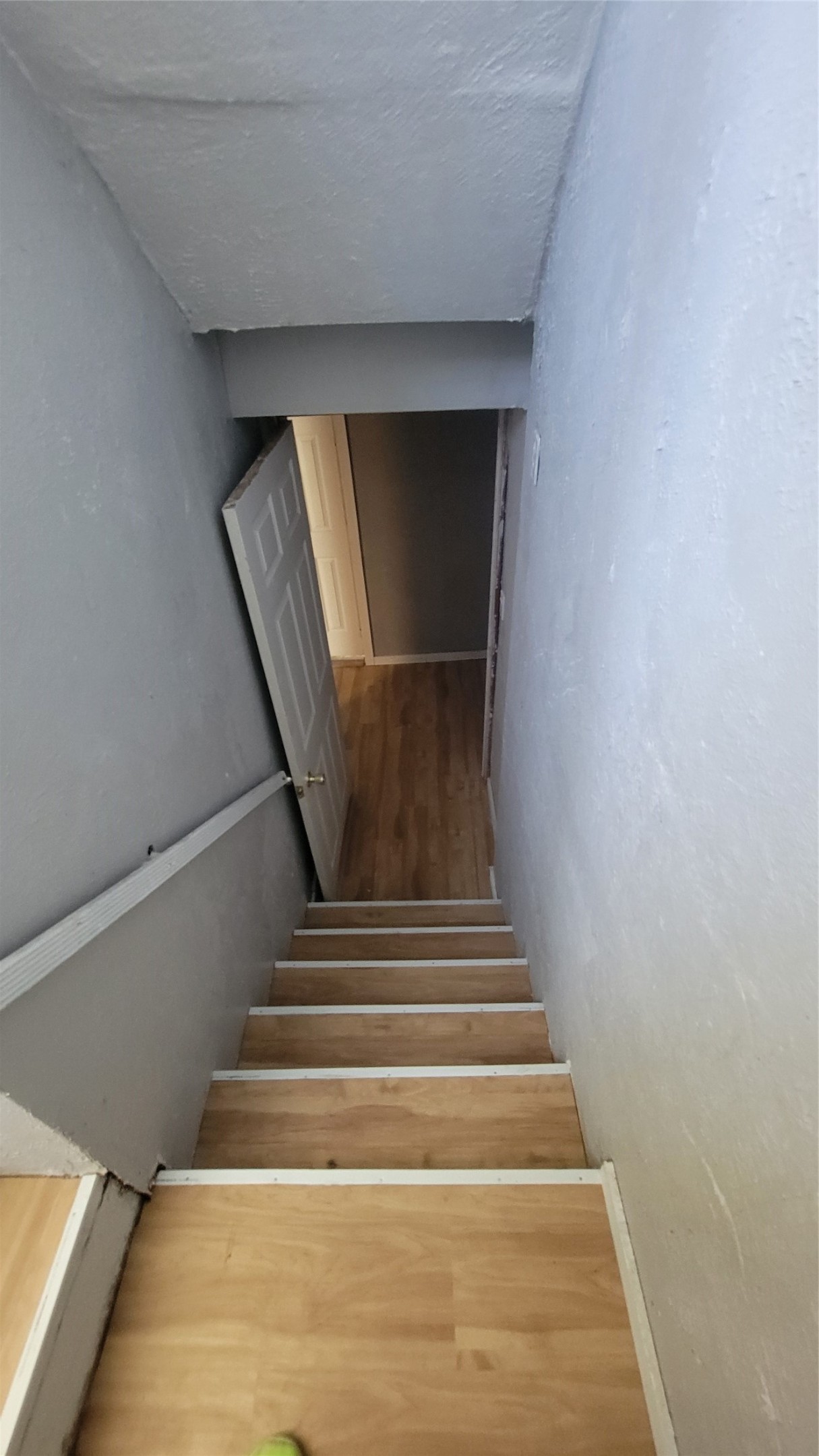 This photo shows a narrow staircase with wooden steps leading down to a lower level, featuring a door at the bottom. The walls are painted a light color, and there's a handrail on one side.