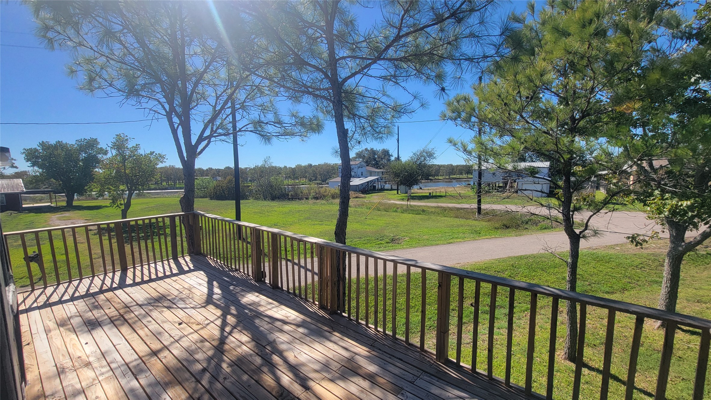 Spacious wooden deck overlooking a lush, green yard with mature trees, providing a serene and private outdoor space. Ideal for relaxation and enjoying nature.