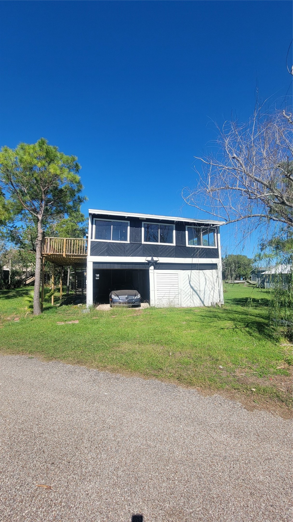 Elevated home with a two-car garage underneath, featuring a sunroom and a side deck. Surrounded by lush greenery, perfect for enjoying nature.