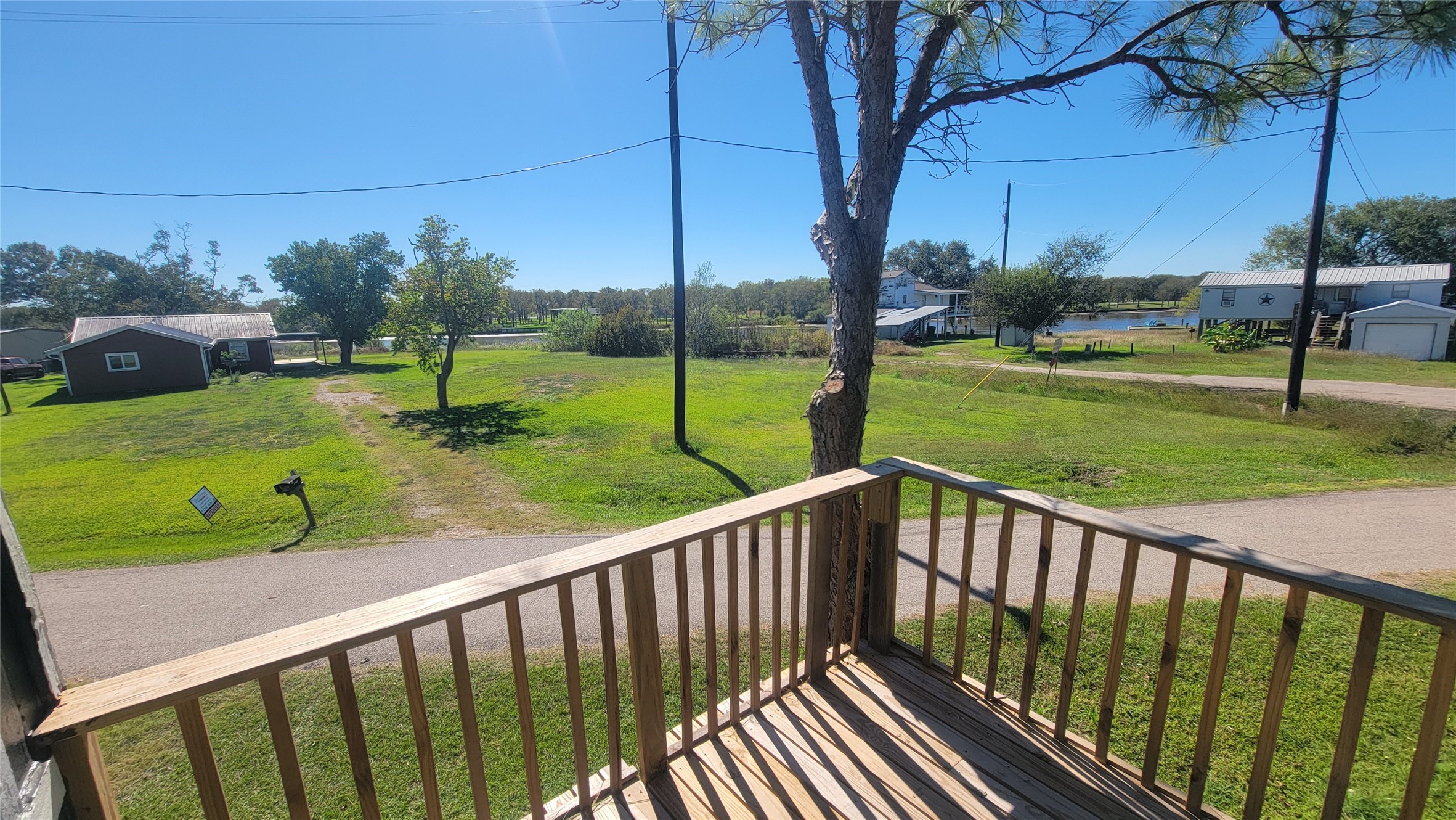 Charming neighborhood view from a cozy wooden balcony, overlooking a grassy area with a clear sky and nearby houses. Ideal for enjoying peaceful outdoor moments.