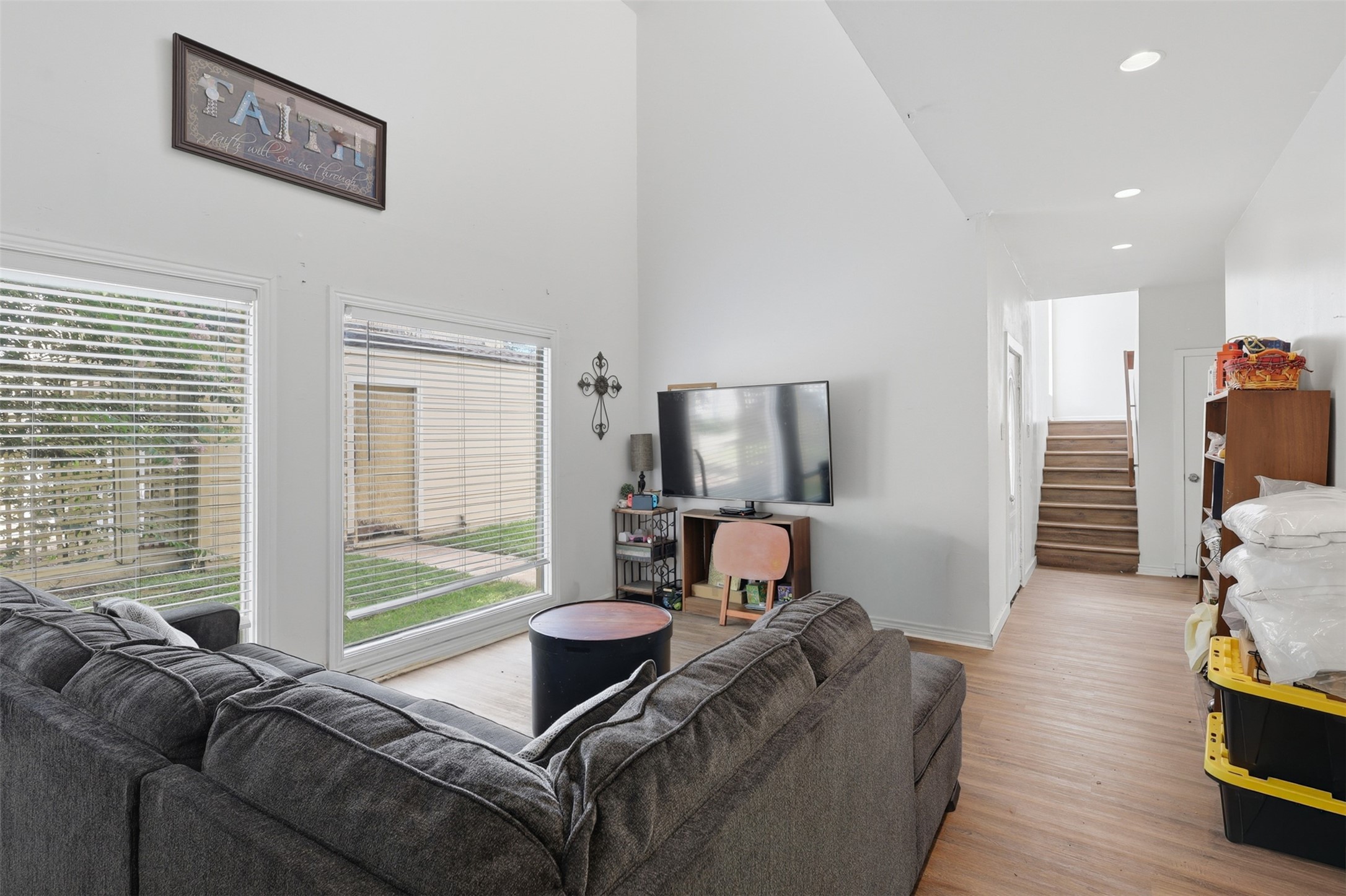 High double-height ceilings meet expansive oversized windows, casting beautiful natural light across warm wood-style flooring and guiding the way to the upper level.
