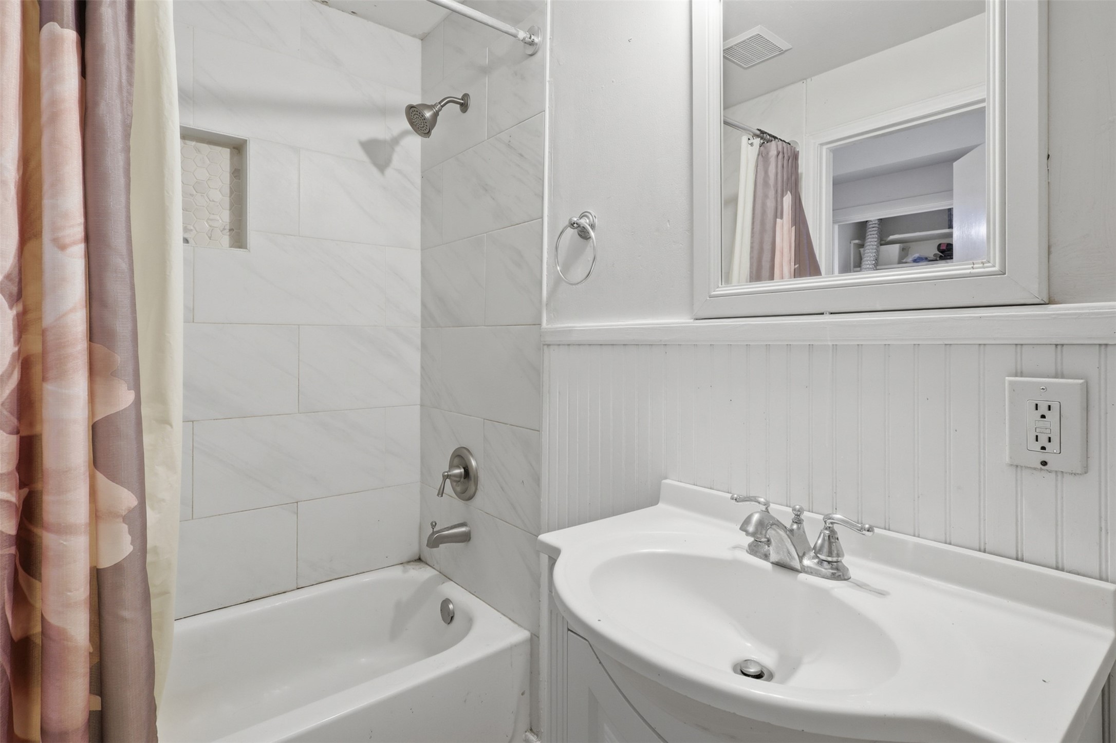 Tastefully updated shower area featuring modern large-format tile surround, recessed storage niche, and classic beadboard accents.