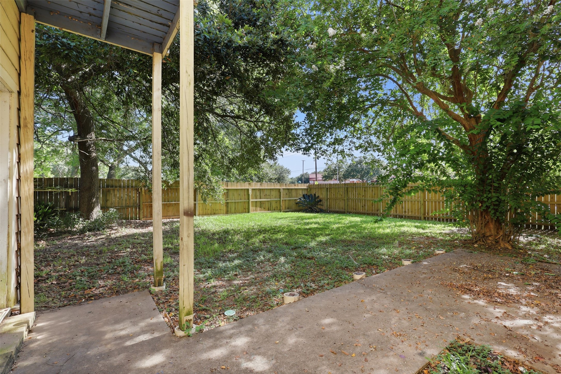 Sheltered concrete patio pad offers a comfortable outdoor seating zone framed by private fencing and mature surrounding foliage.