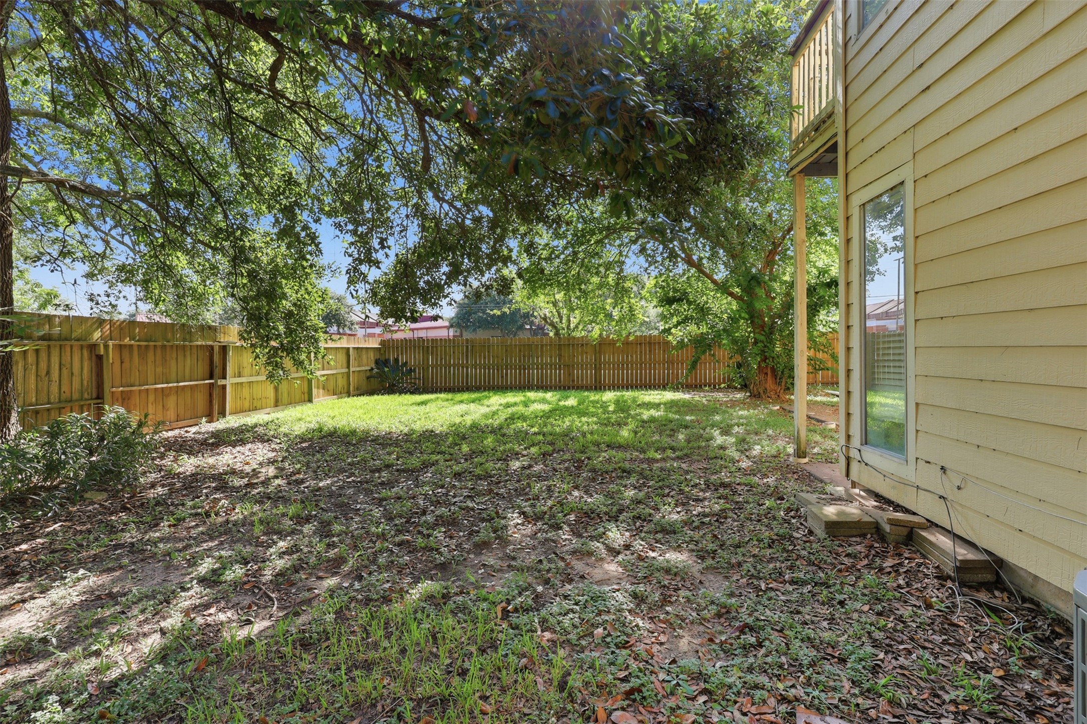 Broad canopy trees provide refreshing, cool shade across a fully enclosed back yard ideal for pets, play, or custom landscaping projects.