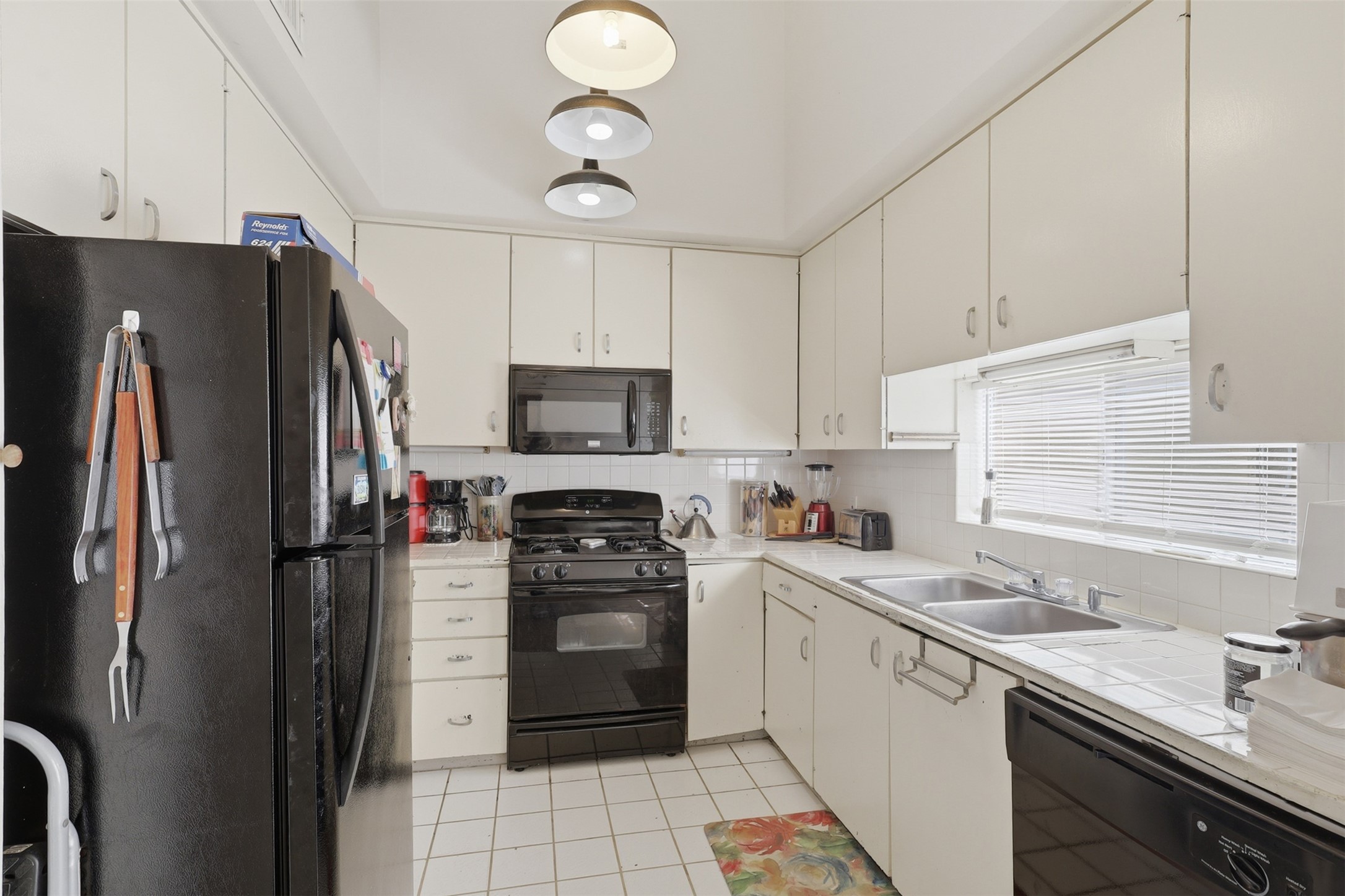 Bright overhead pendant lighting illuminates abundant white cabinetry and seamless counter space, ideal for easy daily meal prep.