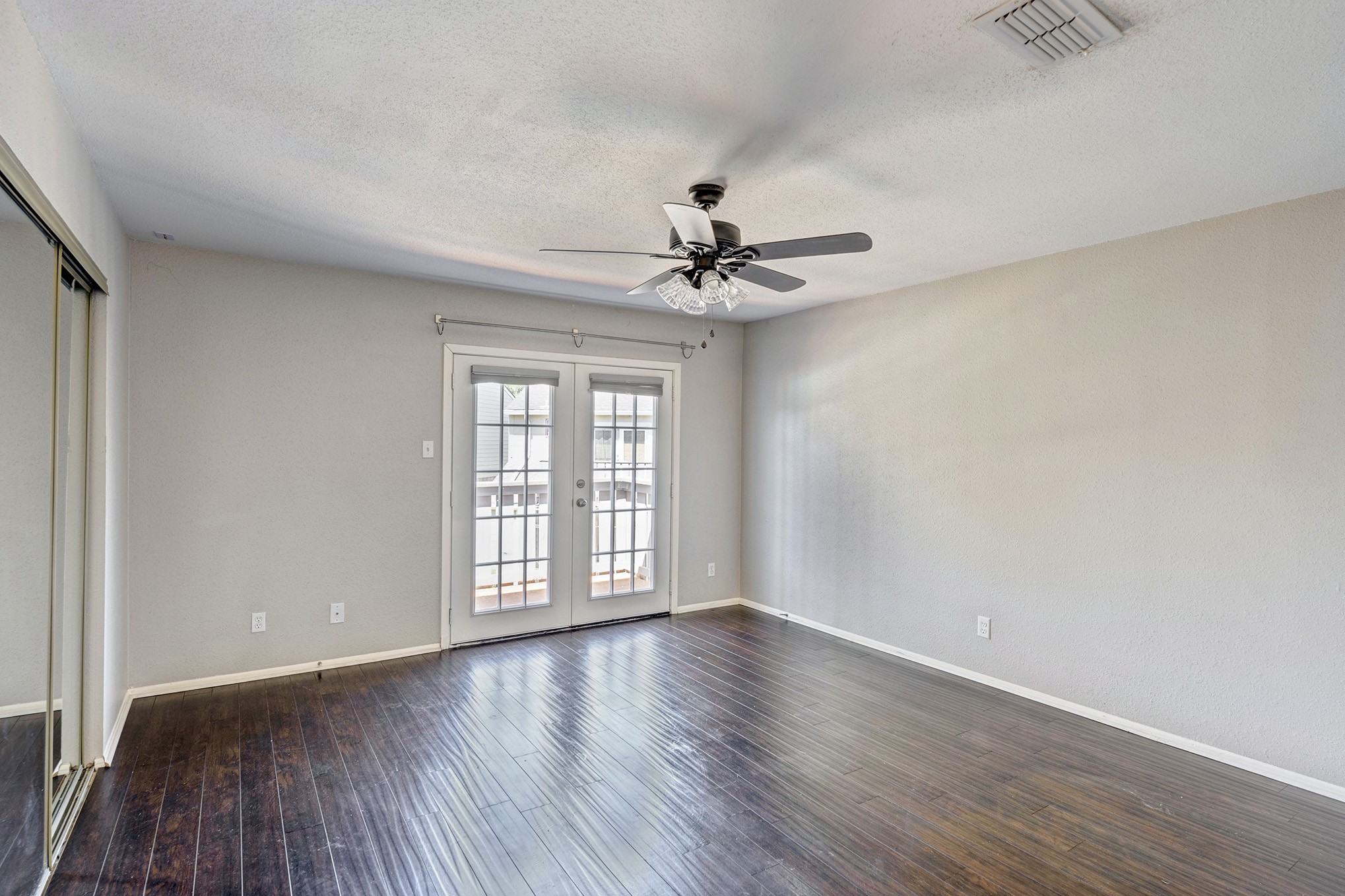 Back bedroom with french doors to the balcony, mirrored sliding closet doors and ceiling fan.