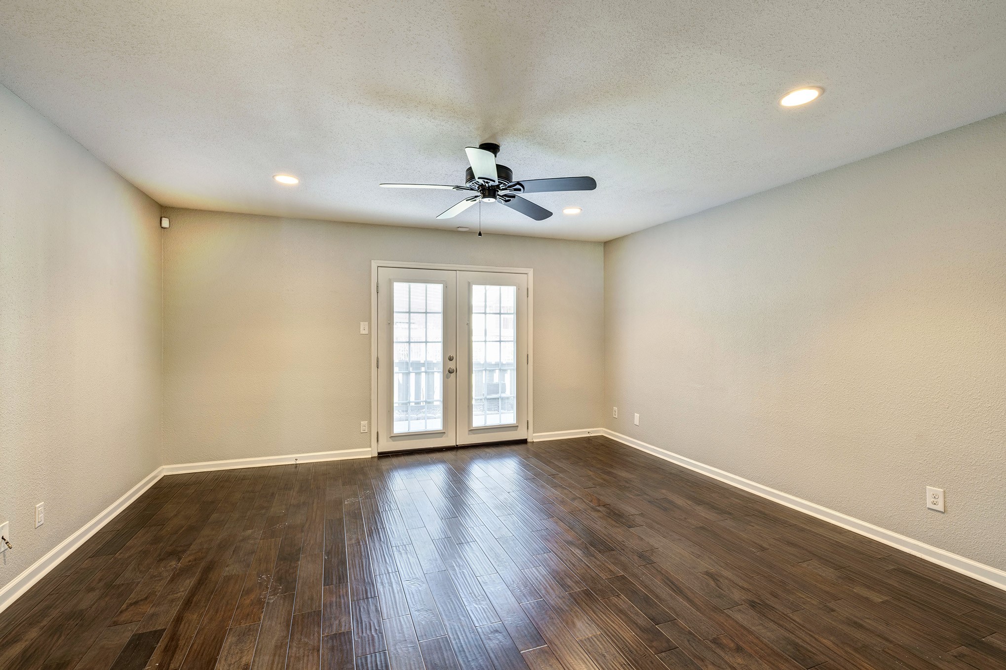 Spacious living room with engineered wood flooring, ceiling fan and recessed lighting. French doors open to the back patio.